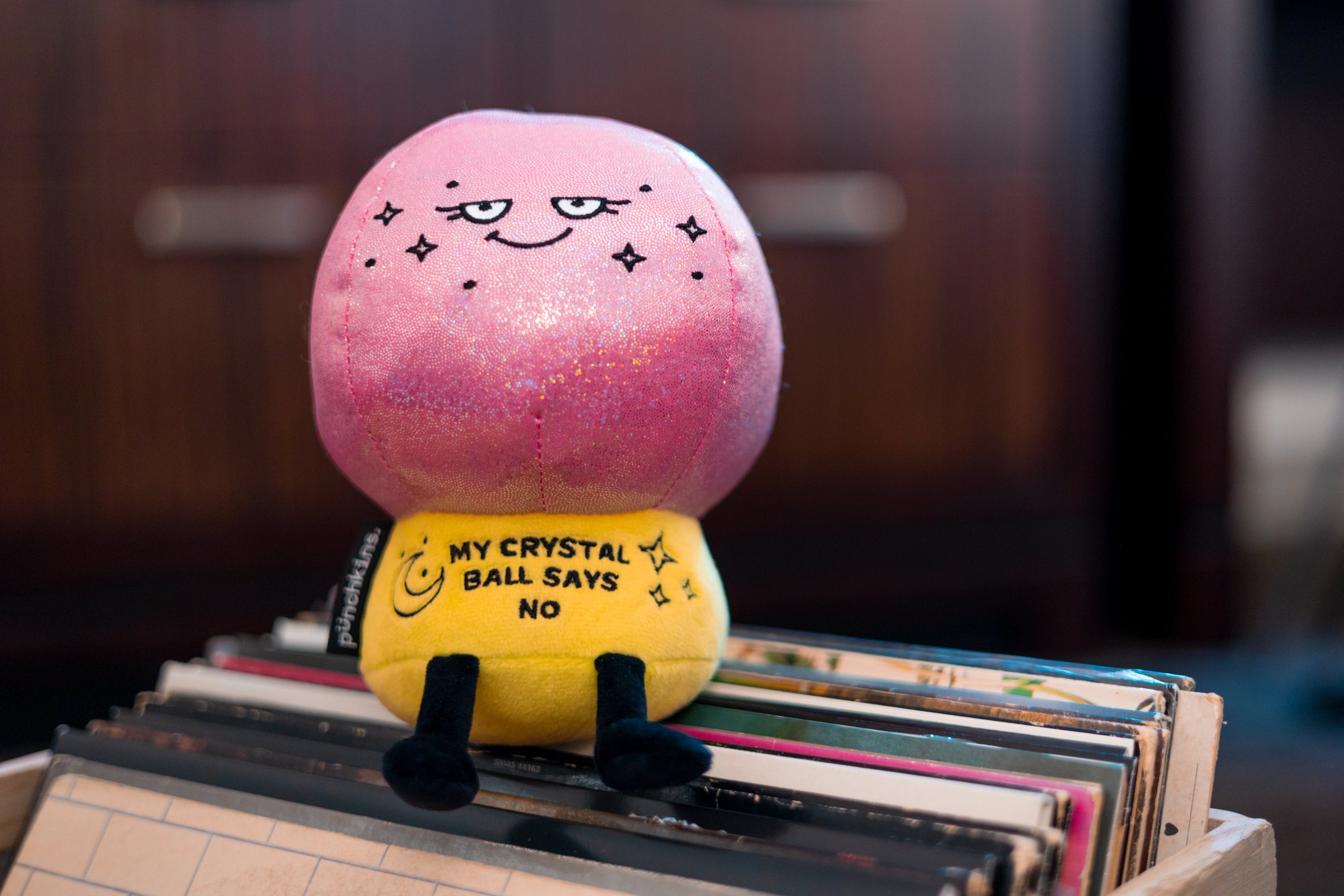 A plush resembling a crystal ball that reads 'MY CRYSTAL BALL SAYS NO' placed on a stack of records.