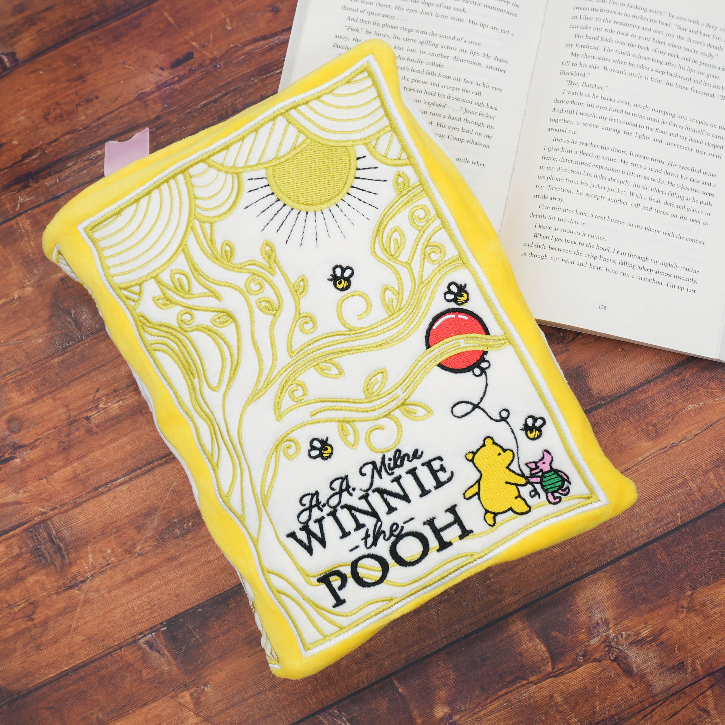 Winnie the Pooh book plush on a wooden surface with an open book in the background