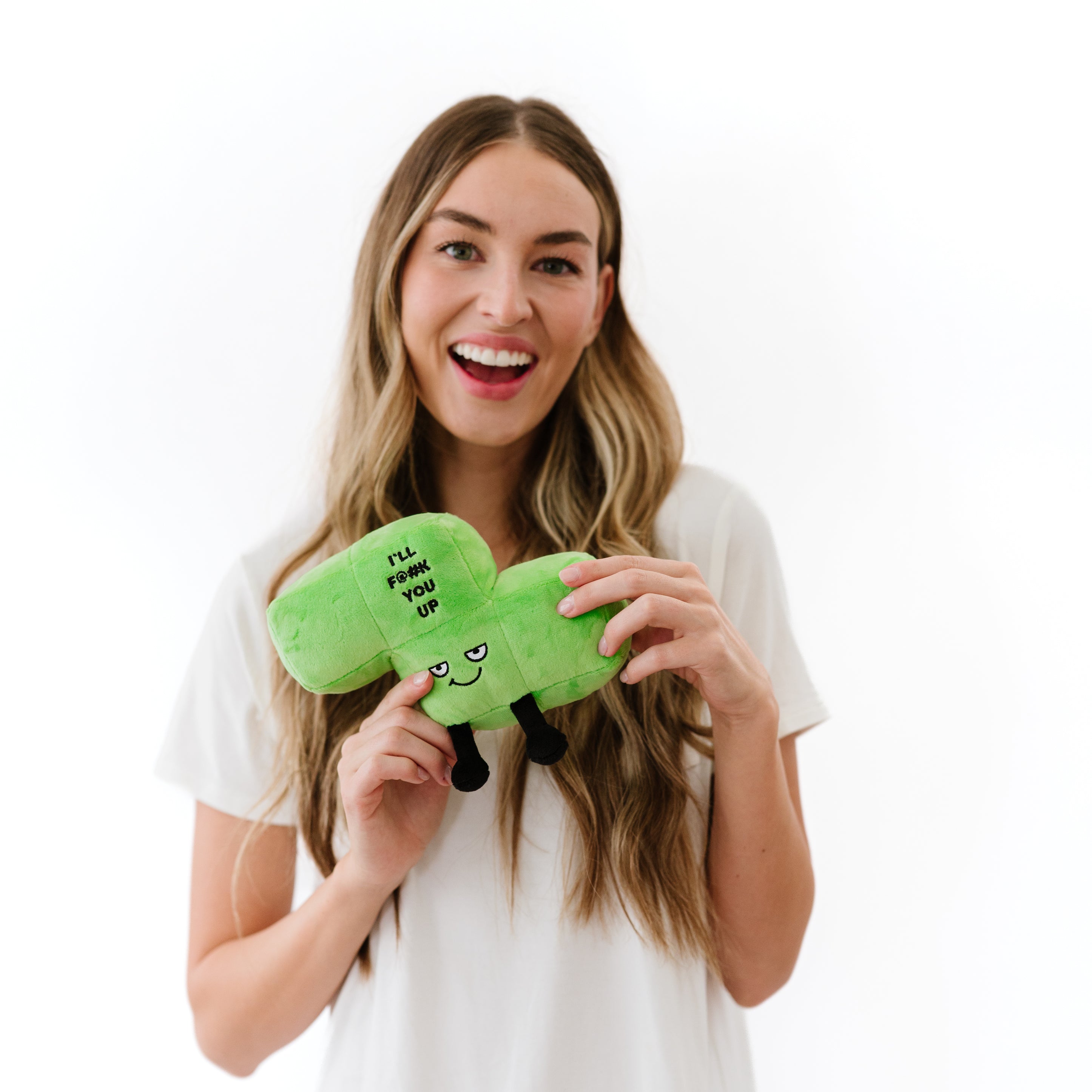 A woman holding a plush designed to look like a green block with a mischievous expression and the phrase 'I'll F@#K you up' written on it.
