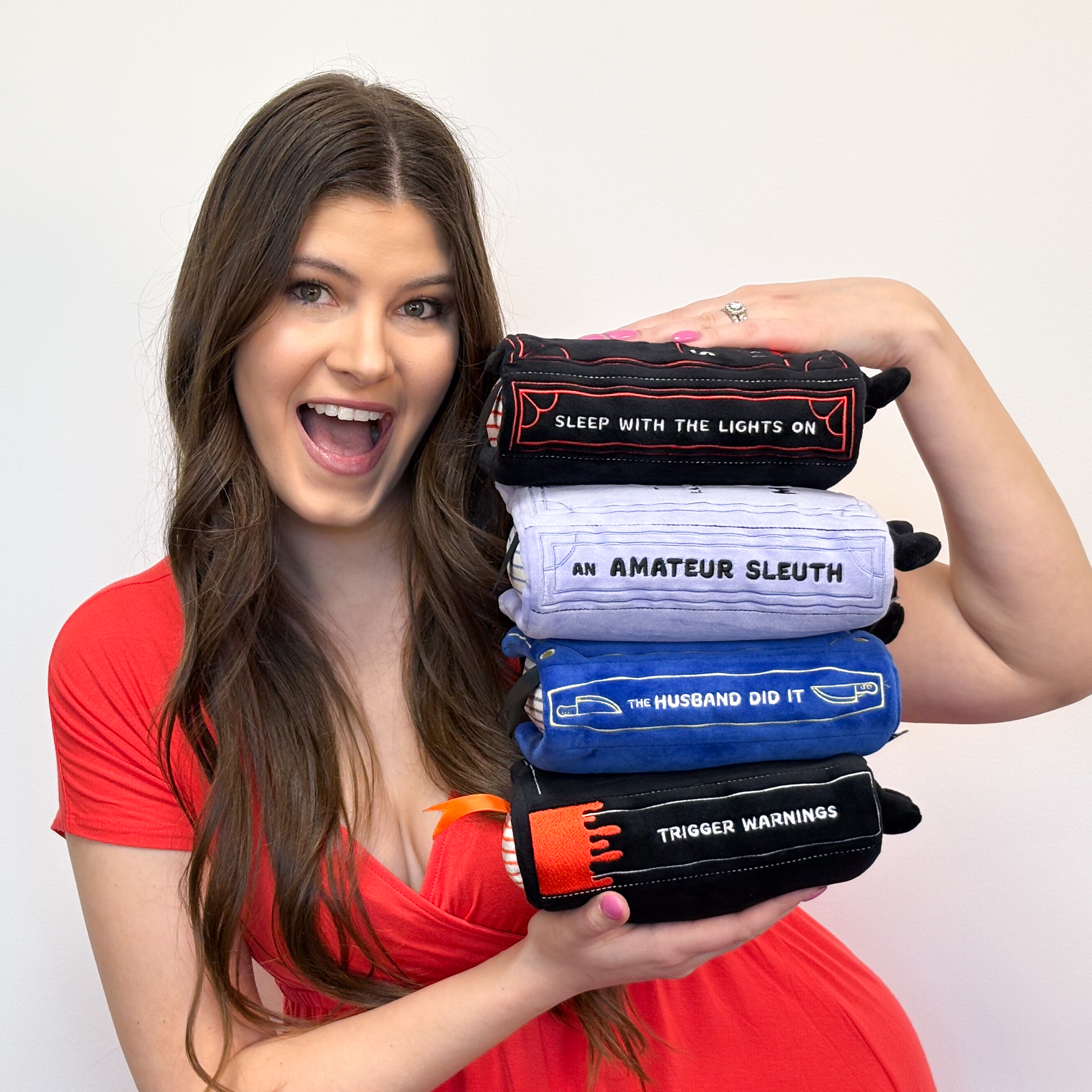 Brunette holding a stack of thriller, horror, and mystery book plushies
