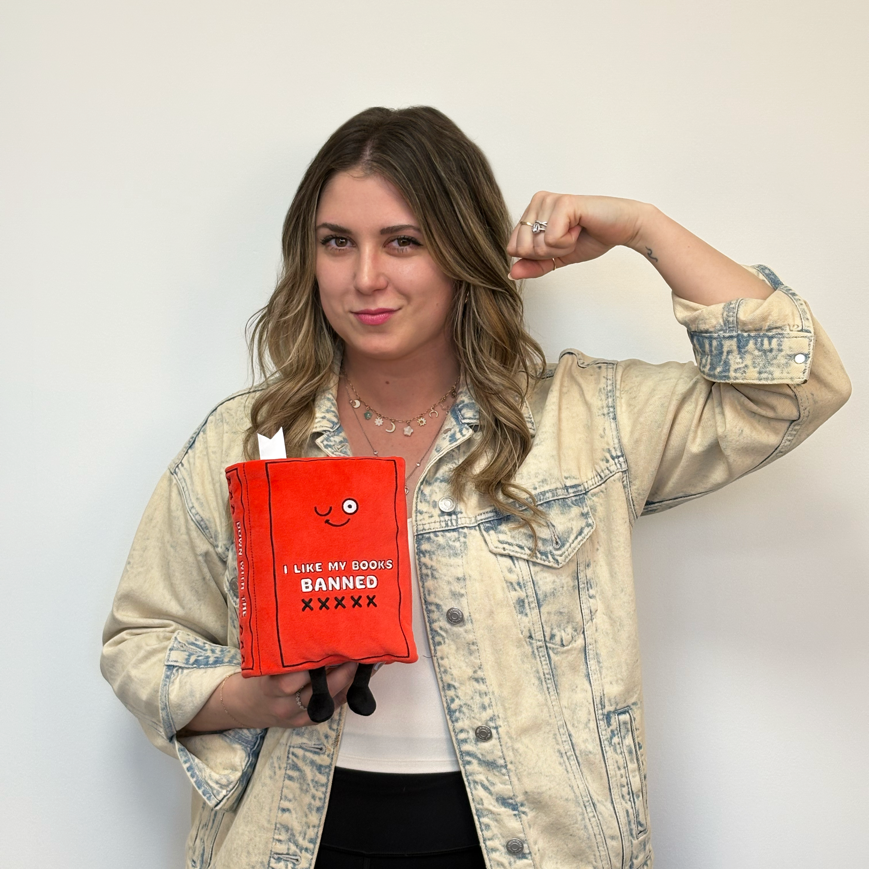 Blonde woman holding red plush book with the text 'I LIKE MY BOOKS BANNED' on its cover.