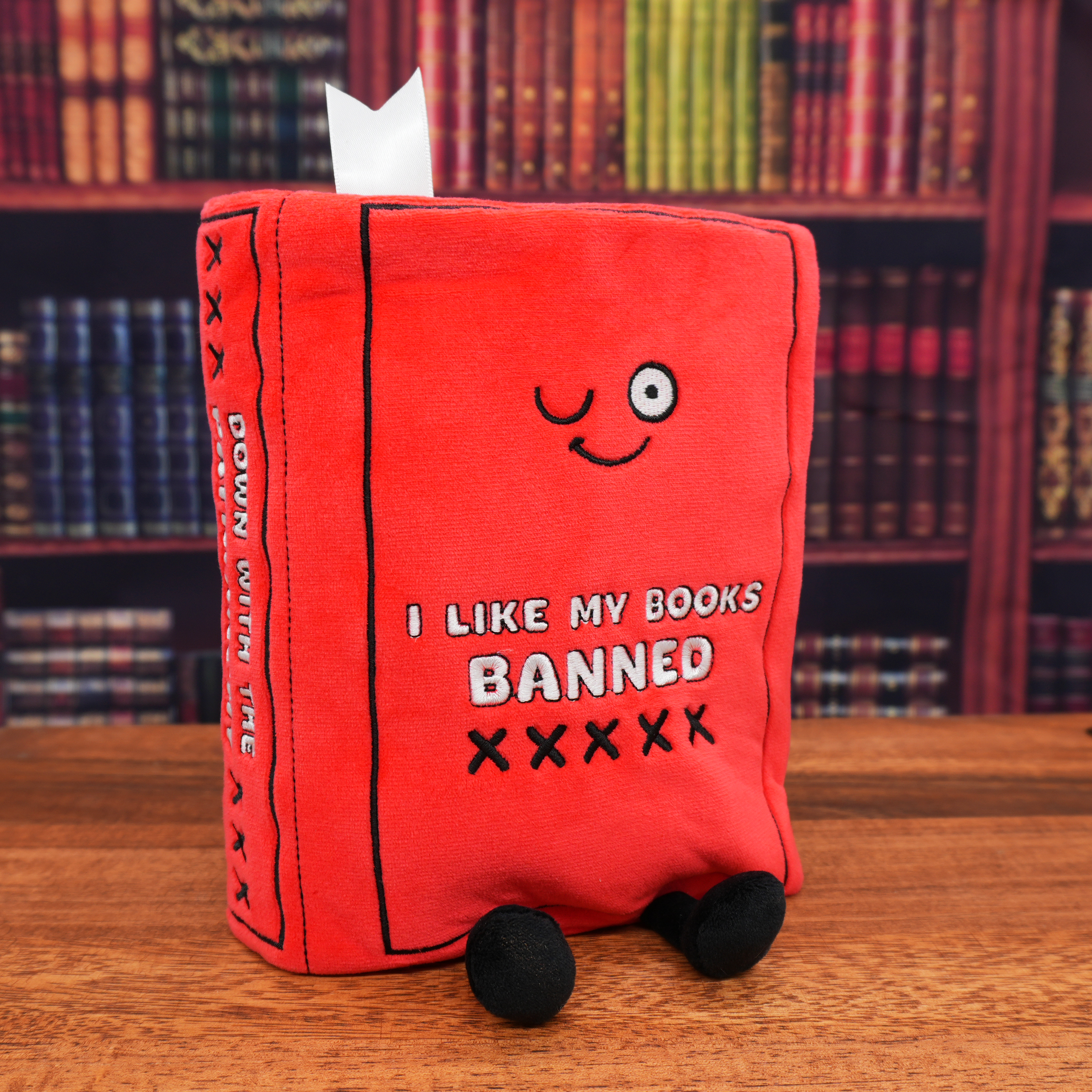 Red plush book with text and a smiley face, set against a bookshelf background.