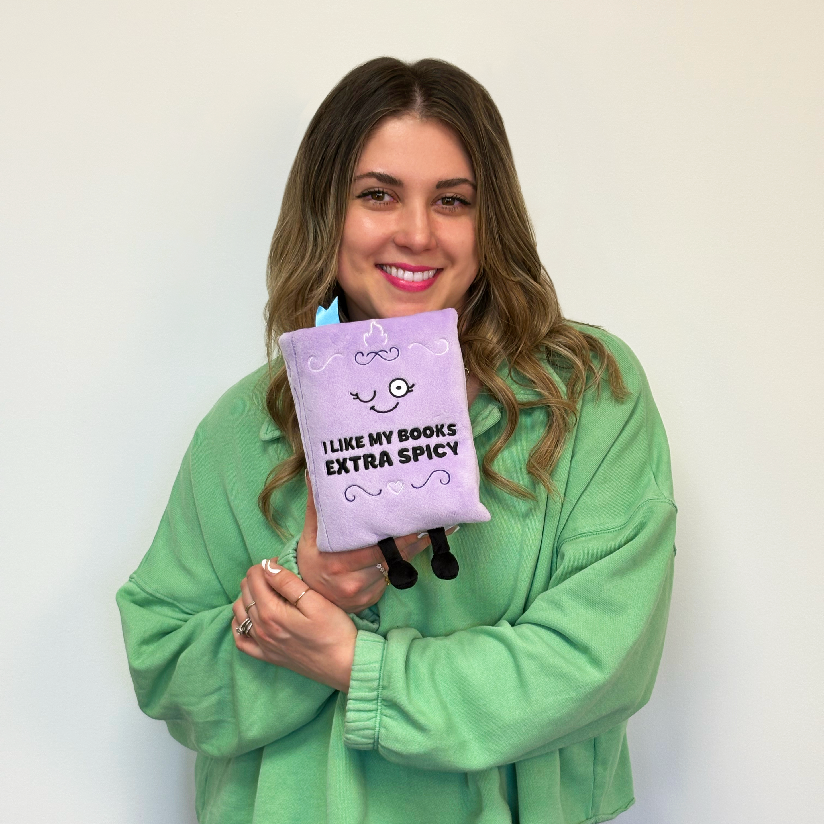 A woman holding a purple book plush with text 'I like my books extra spicy'.