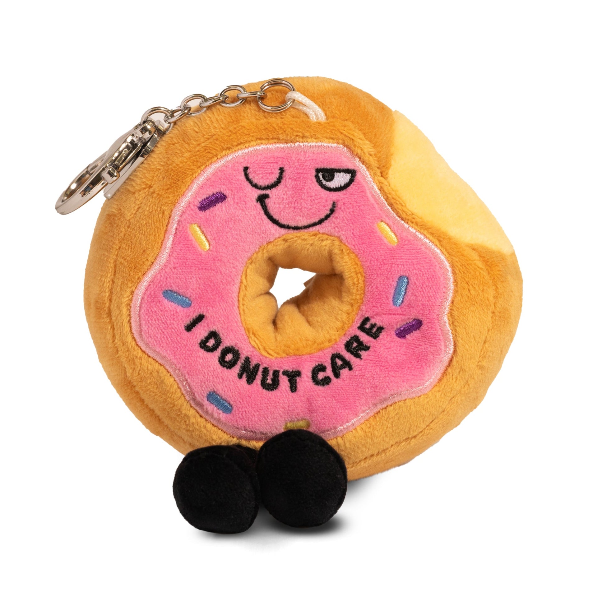 A plush shaped like a donut with a pink icing topping, rainbow sprinkles, and a smiley face with the phrase 'I DONUT CARE' written on the top. It has black dangly legs and is attached to a keychain.