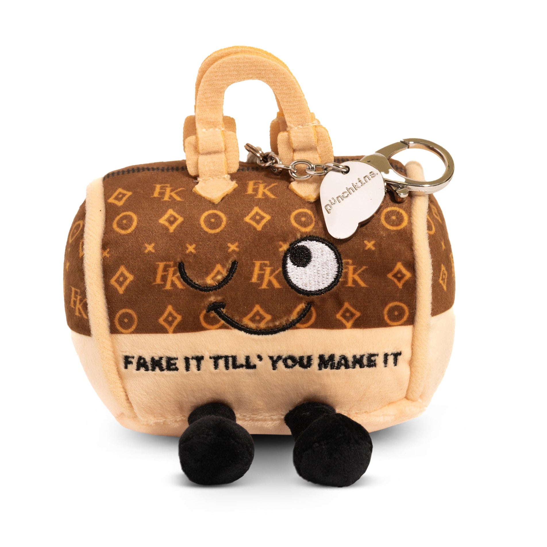 A plush bag charm of a purse with a brown and beige color scheme, featuring a whimsical face and text that reads, "Fake it till you make it."