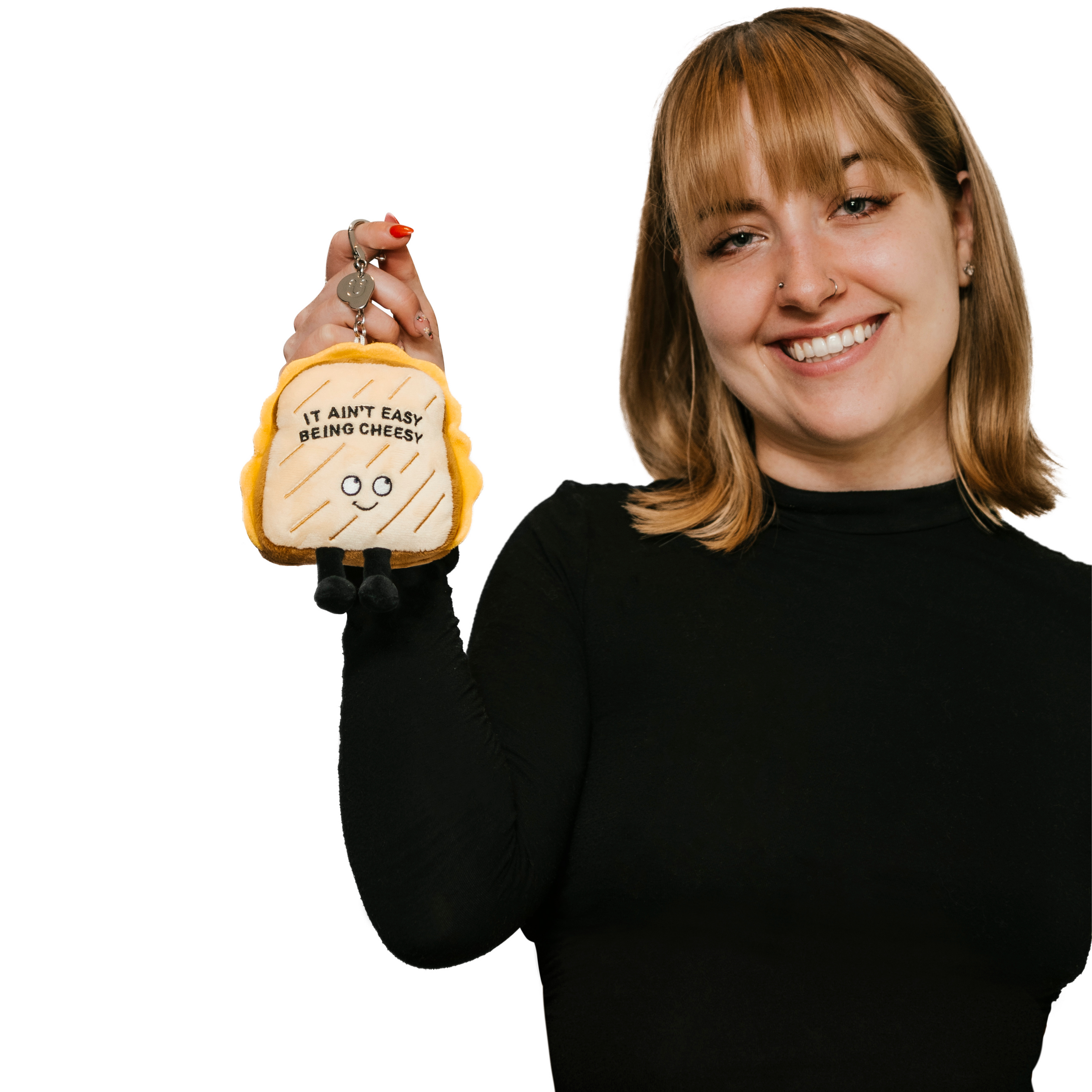 A model holding a plush charm designed to look like a grilled cheese sandwich with the phrase 'It Ain't Easy Being Cheesy' written on it.