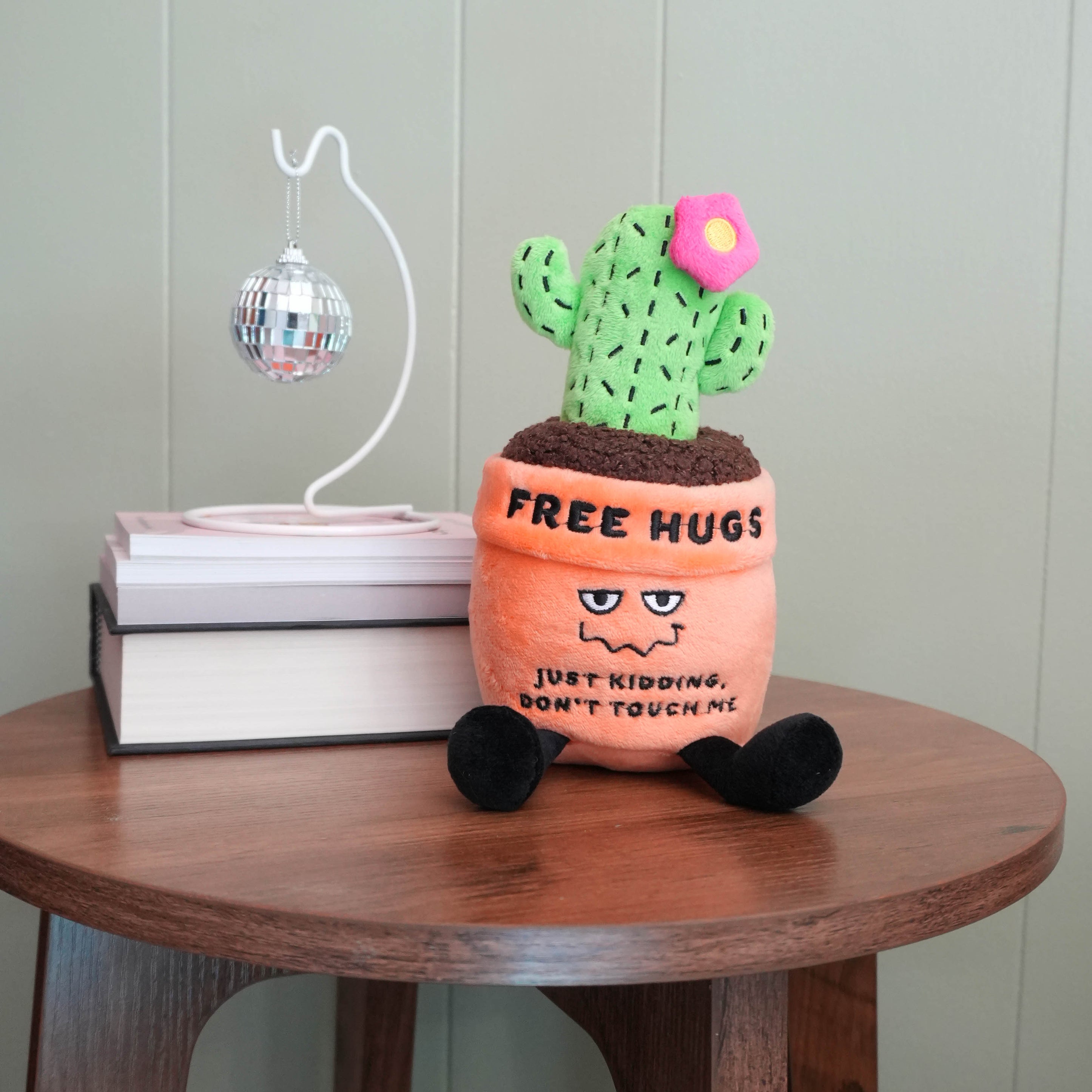 Plush cactus toy with 'Free Hugs' text on a wooden table.