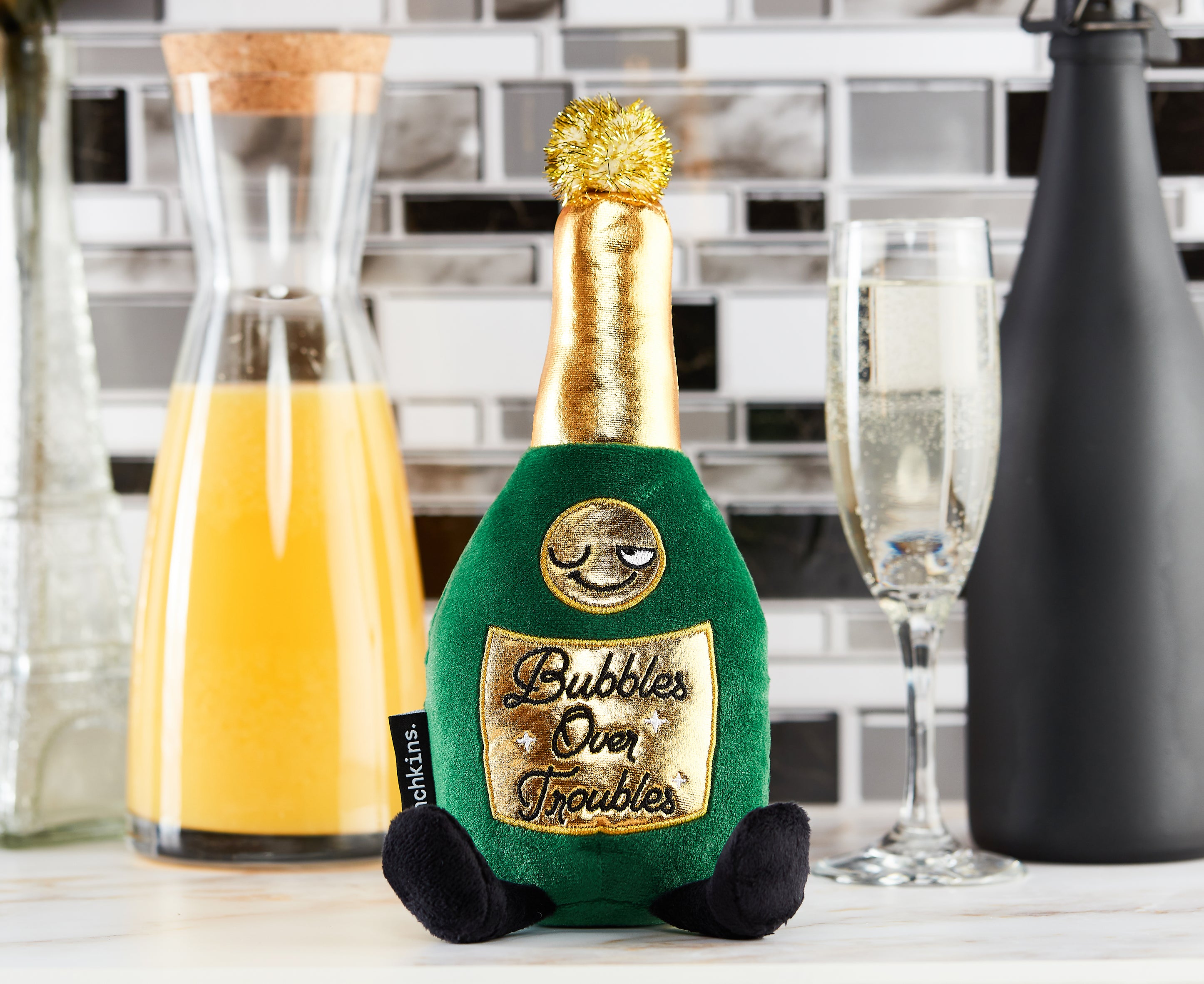 A champagne bottle plush with the text 'Bubbles Over Troubles' printed on it placed in a kitchen.