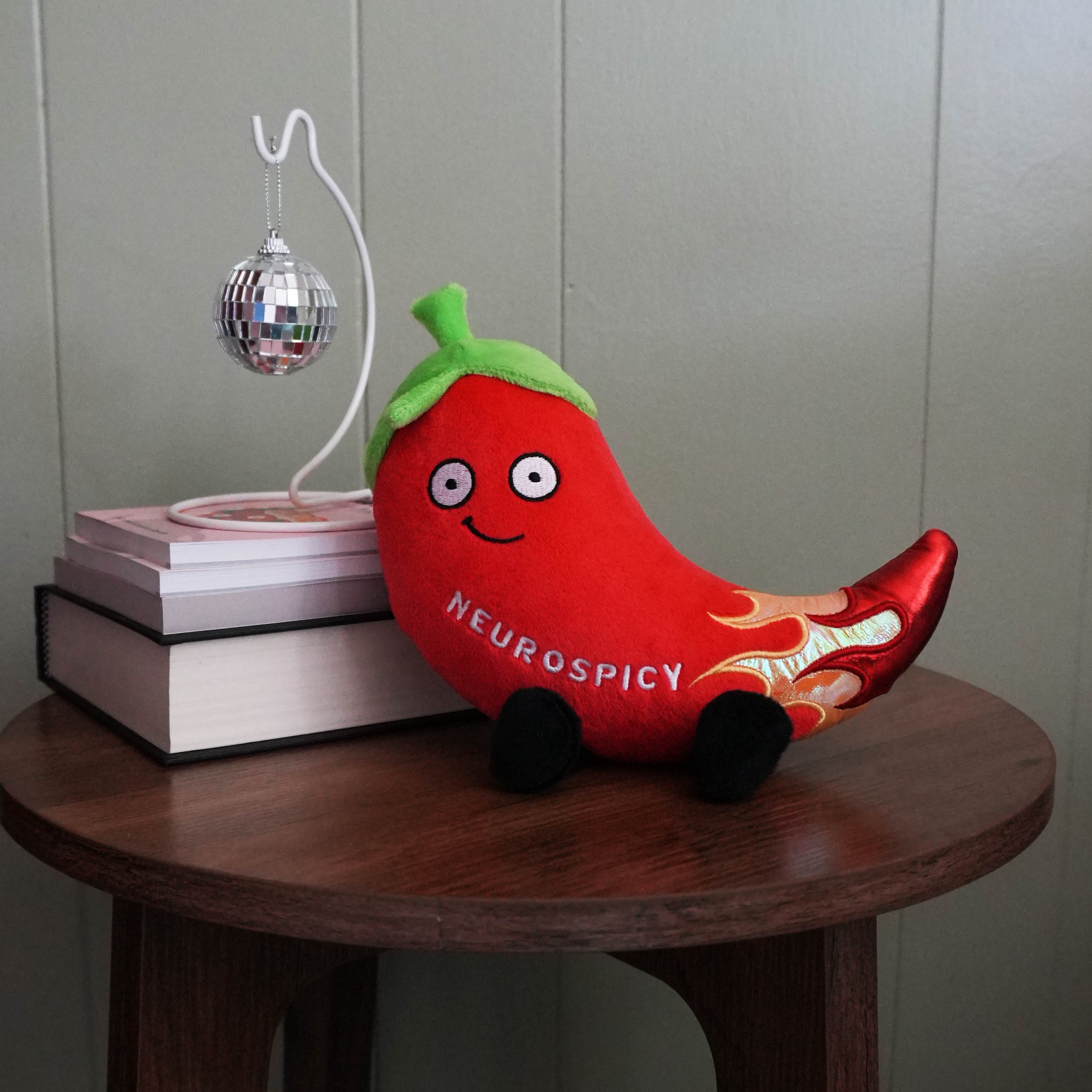 Plush toy chili pepper with 'Neurospicy' branding on a wooden table.