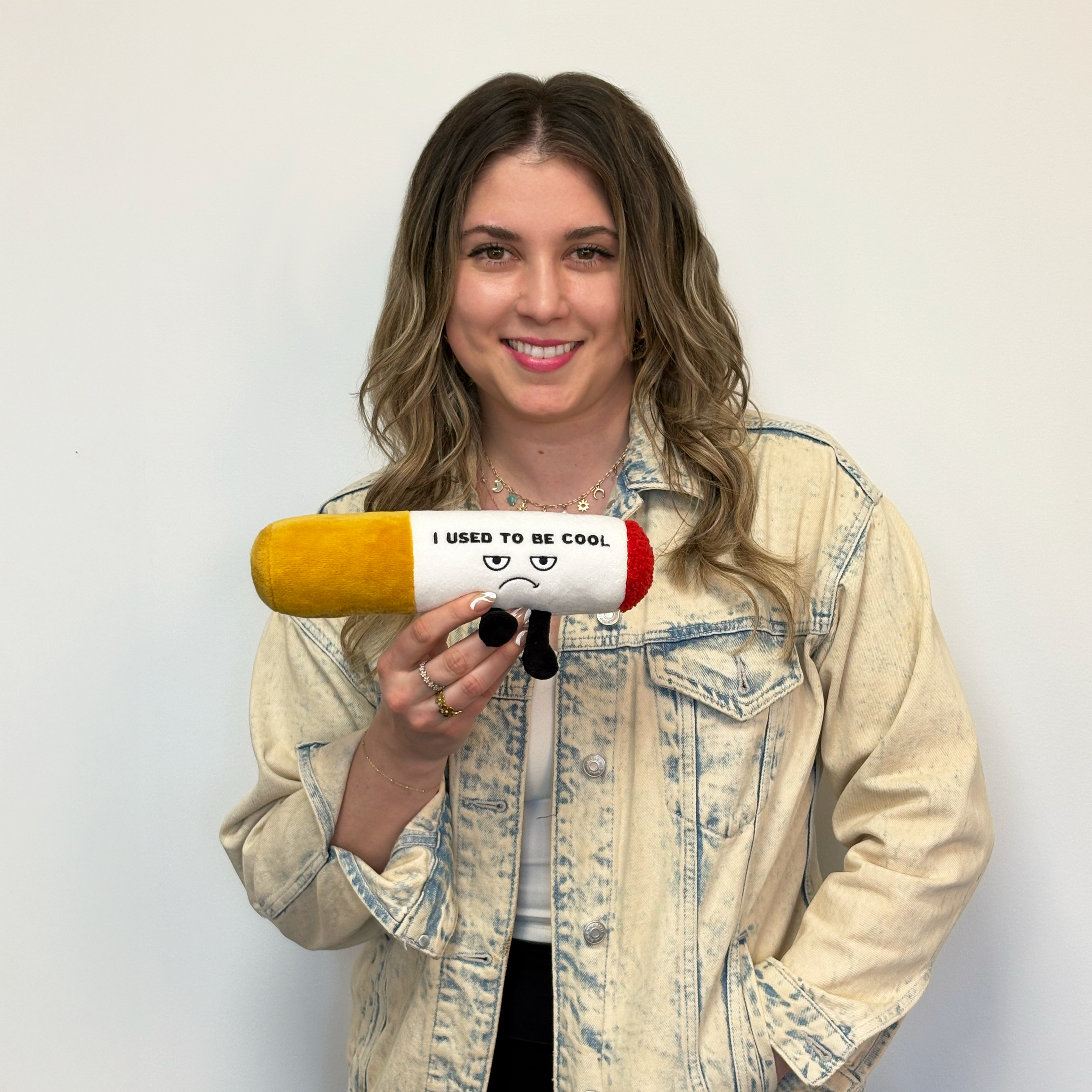 Model holding a plush cigarette with an upset face expression and the text 'I USED TO BE COOL' on it.