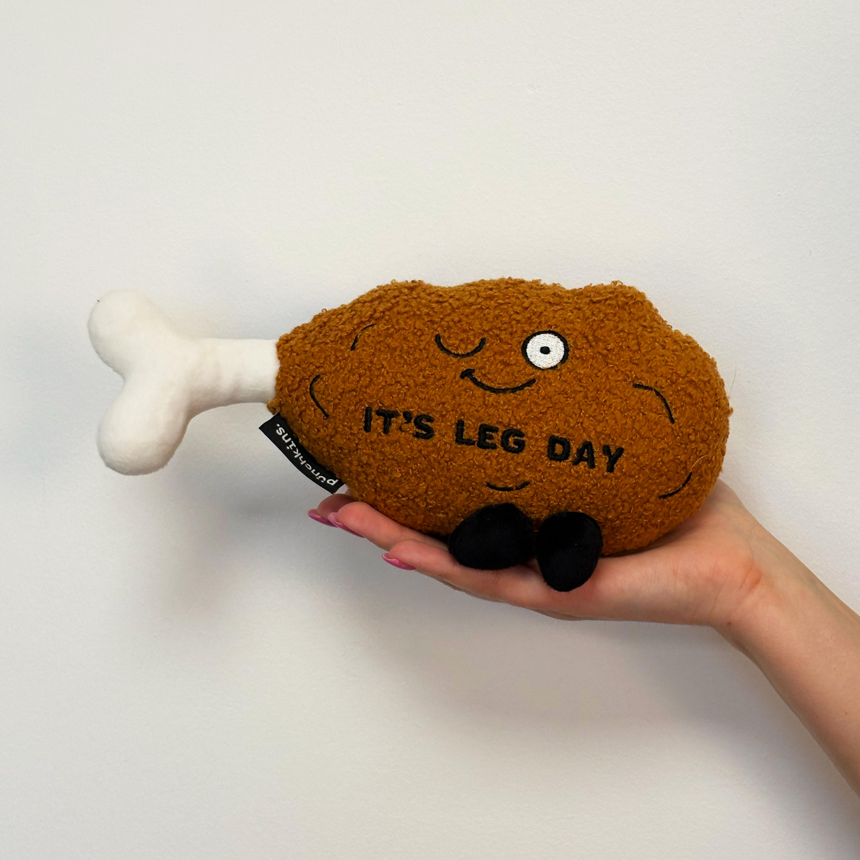 Hand holding a plush chicken leg with a smiling face and the text 'IT'S LEG DAY' on it.