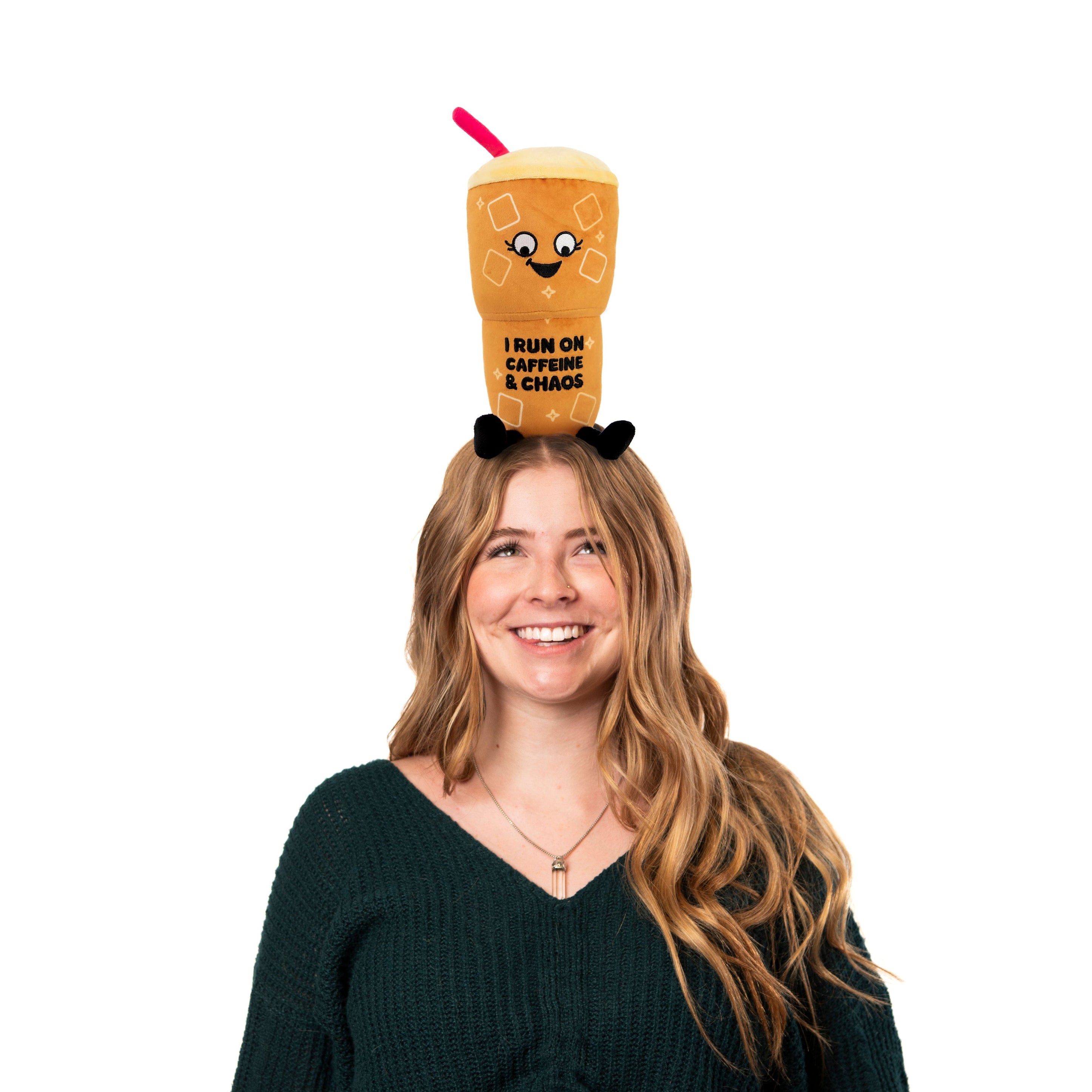 A model with an iced coffee plushie that says, 'I run on caffeine & Chaos' on it.