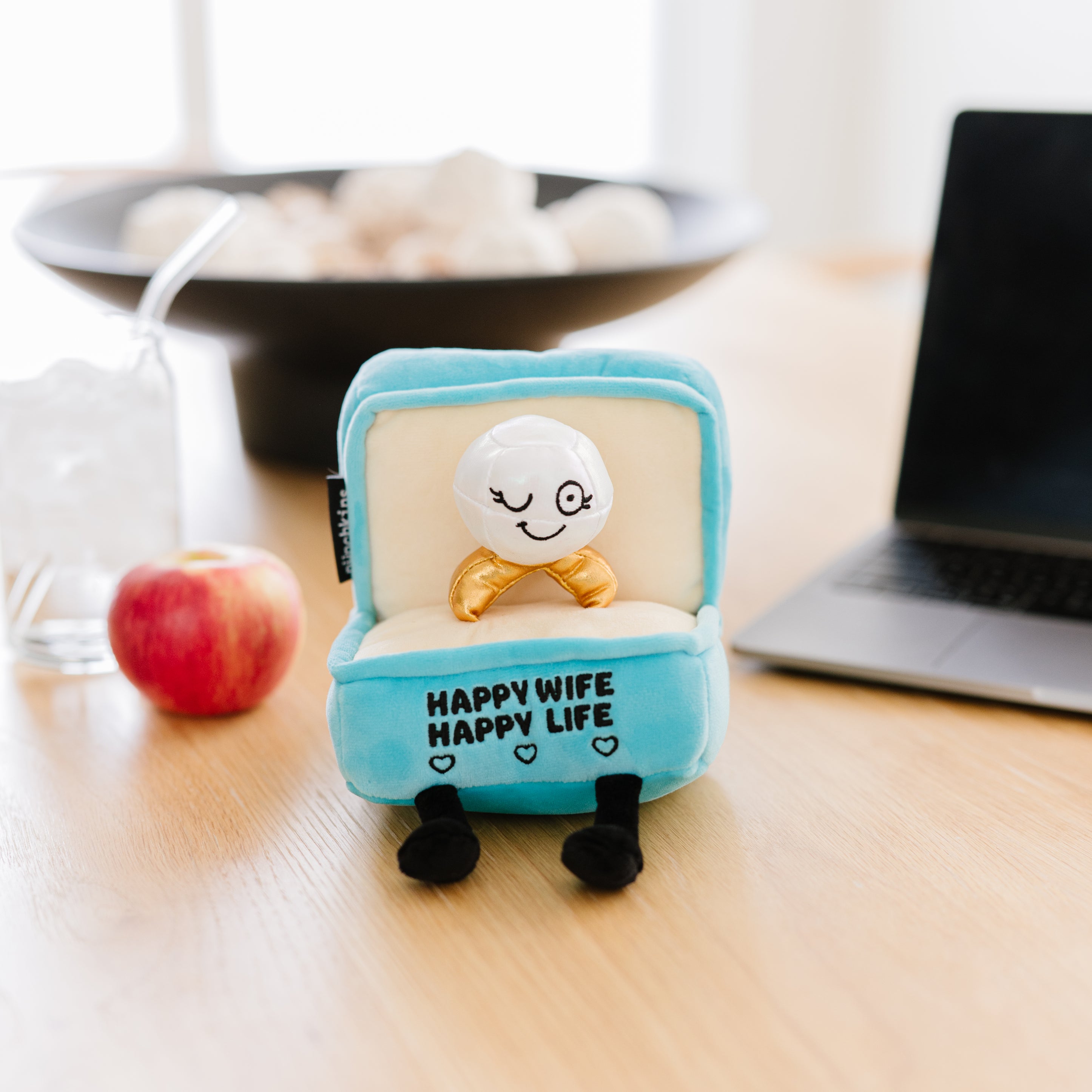 A plush designed to resemble a ring box with the text 'Happy Wife Happy Life' on it, placed on a kitchen table.