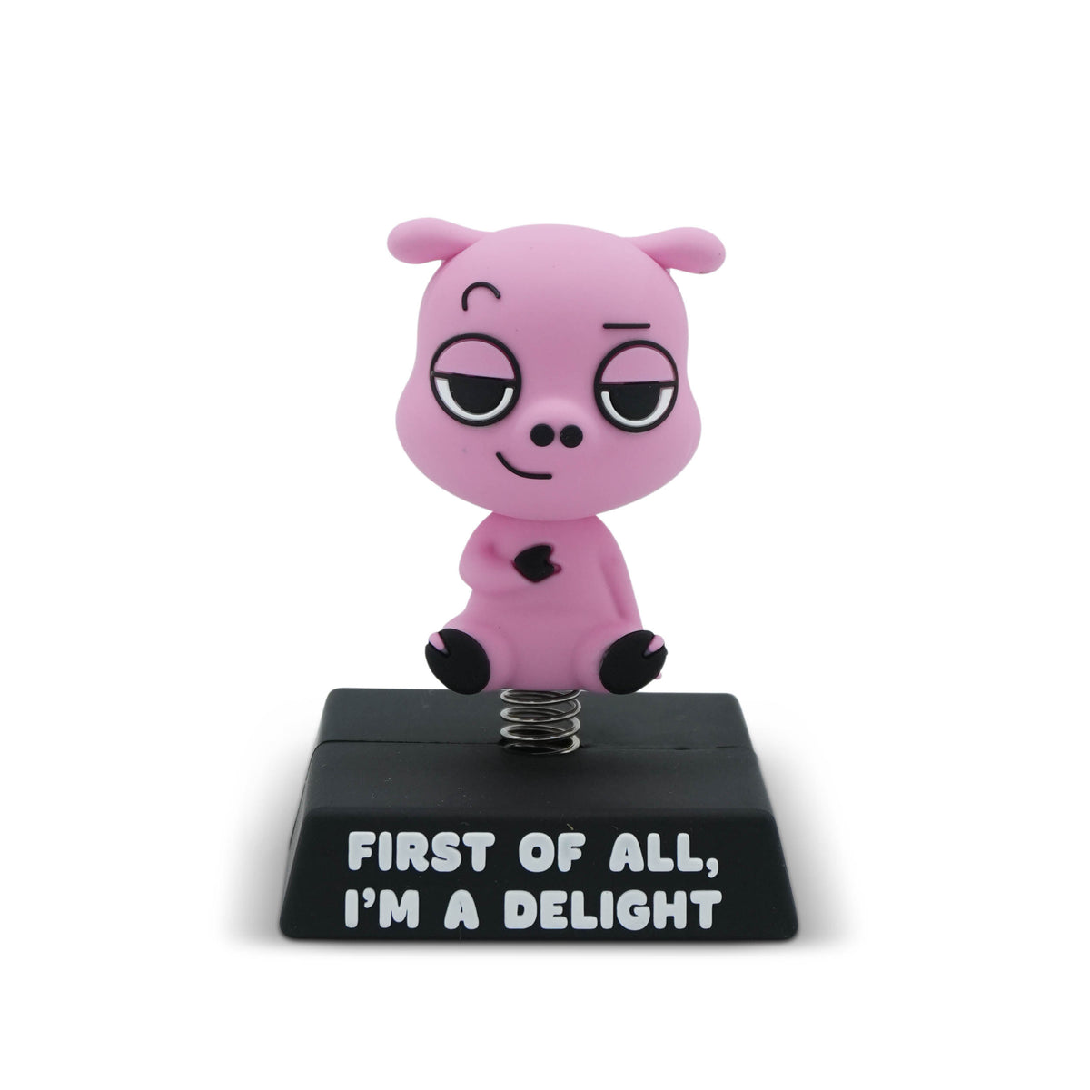 A pink cartoon pig figurine sitting on a black spring-loaded base with the text 'FIRST OF ALL, I'M A DELIGHT' in white lettering, set against a plain white background.