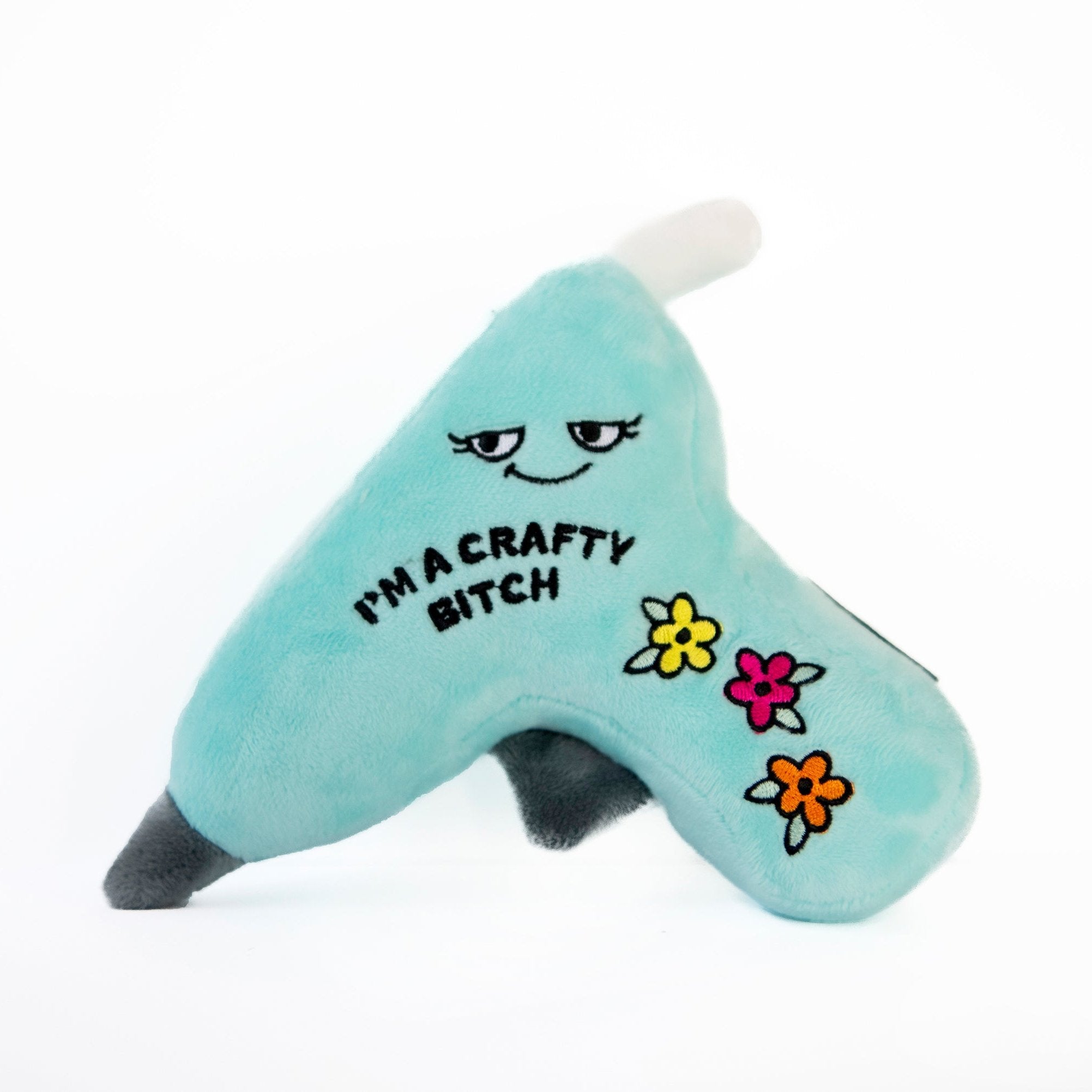 A plushie shaped like a glue gun with a blue body, displaying the text 'I'M A CRAFTY BITCH' on the side, and decorated with colorful flower appliques.
