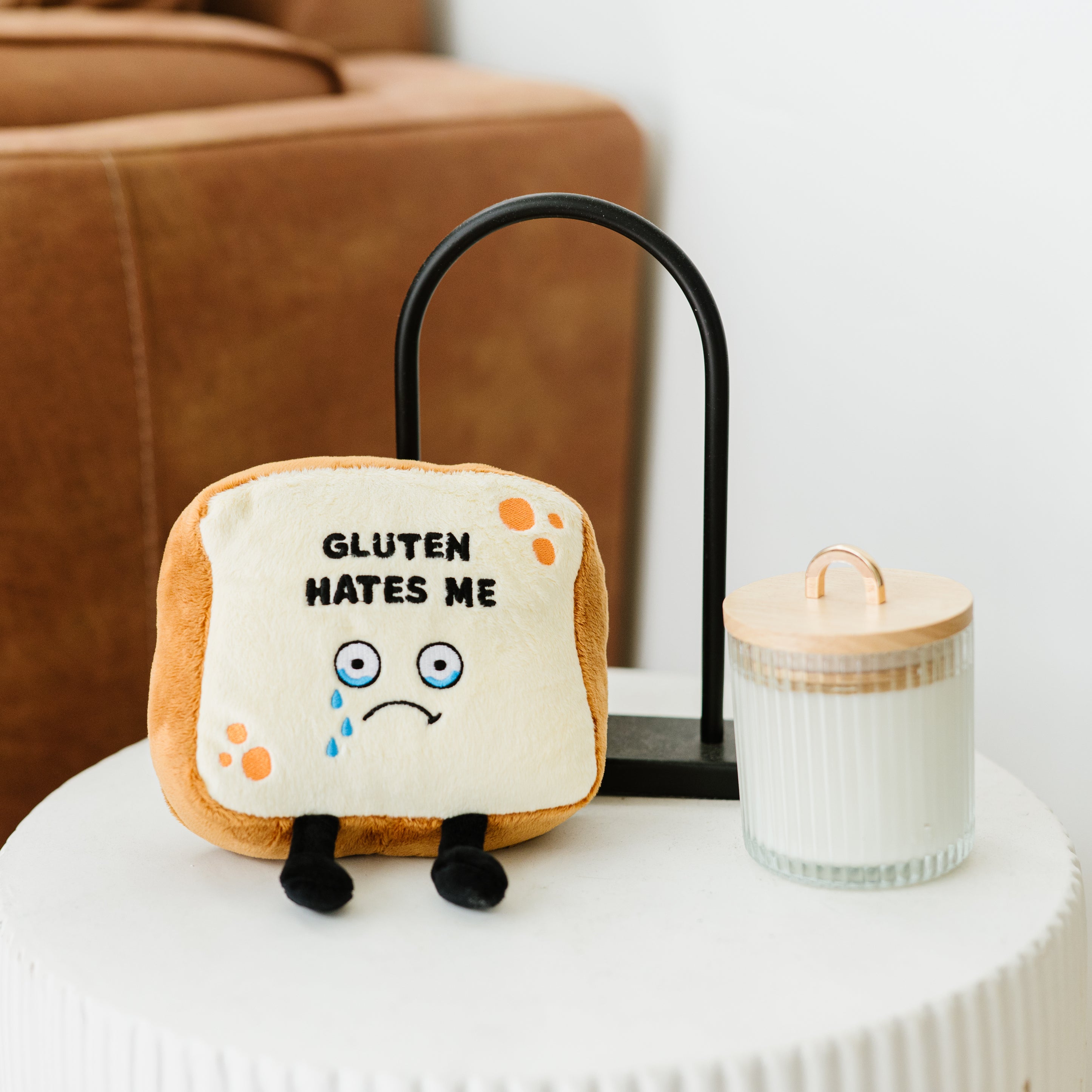 A plush resembling a slice of bread with the phrase 'GLUTEN HATES ME' printed on it placed on a table in the living room.