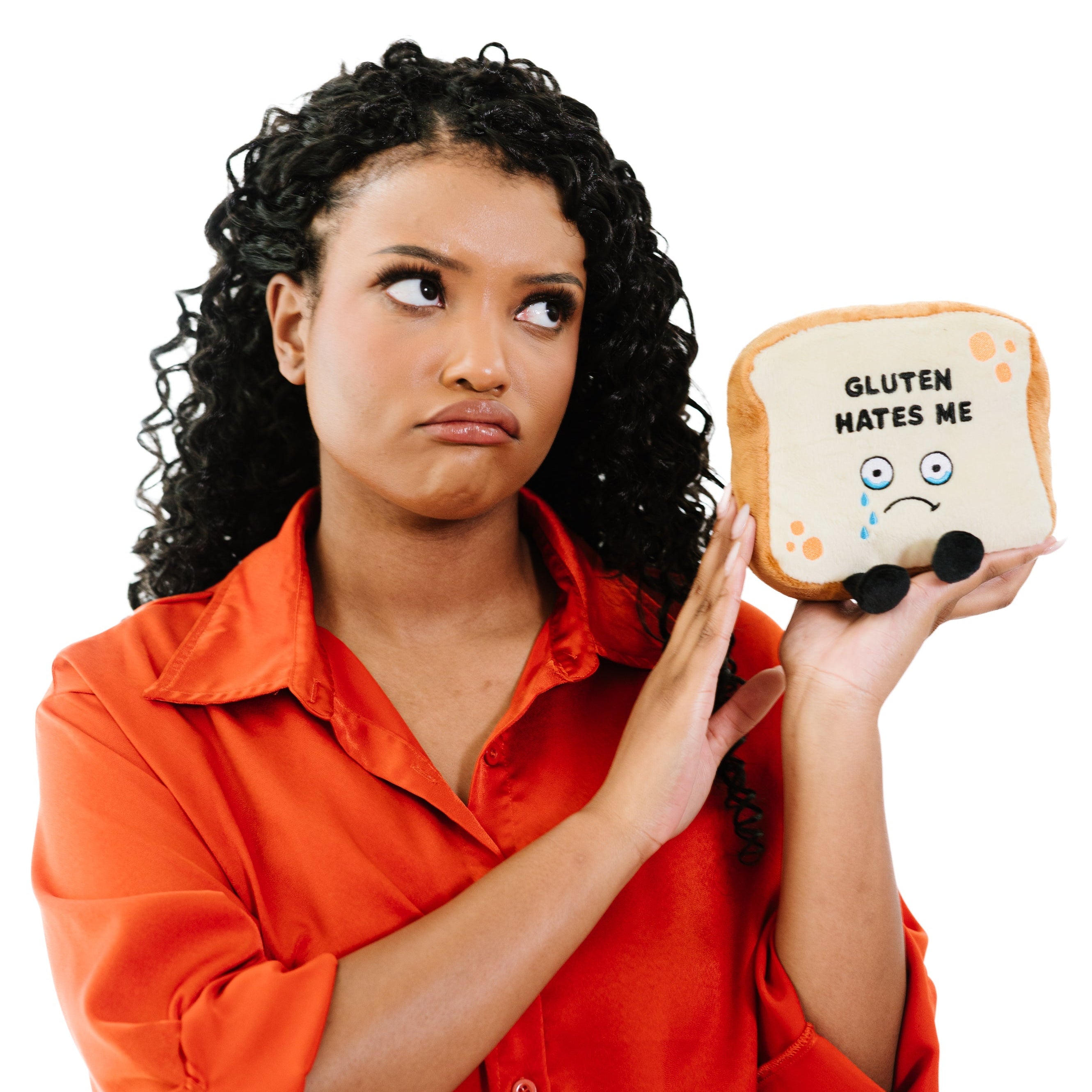 A woman holding a plush resembling a slice of bread with the phrase 'GLUTEN HATES ME' printed on it, with sad facial features and tears depicted on the bread.