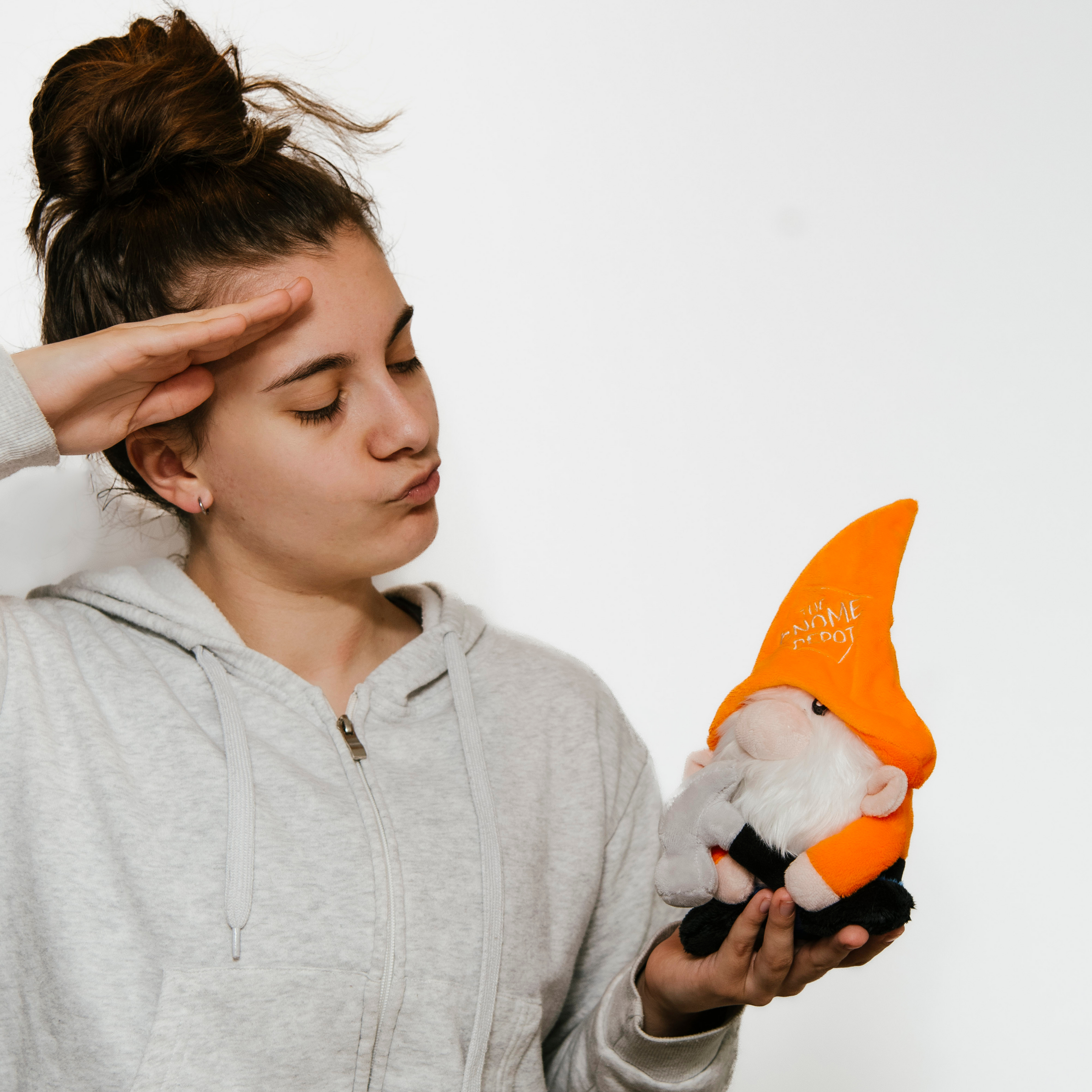 A model holding a plush gnome with a white beard wearing an orange pointy hat with 'The Gnome Depot' written on it.