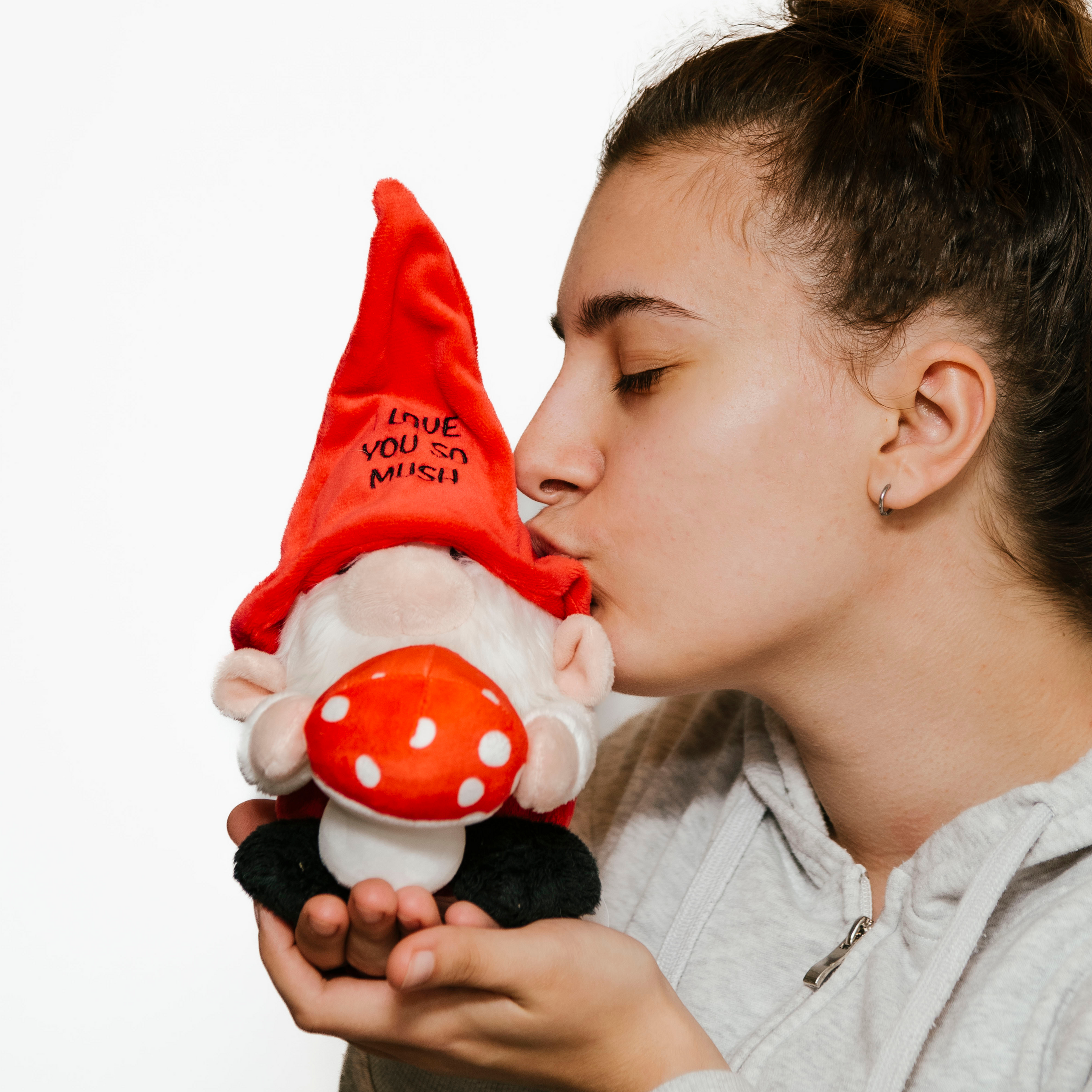 A model is kissing a plush gnome with a red hat with 'I love you so much' text written on it.