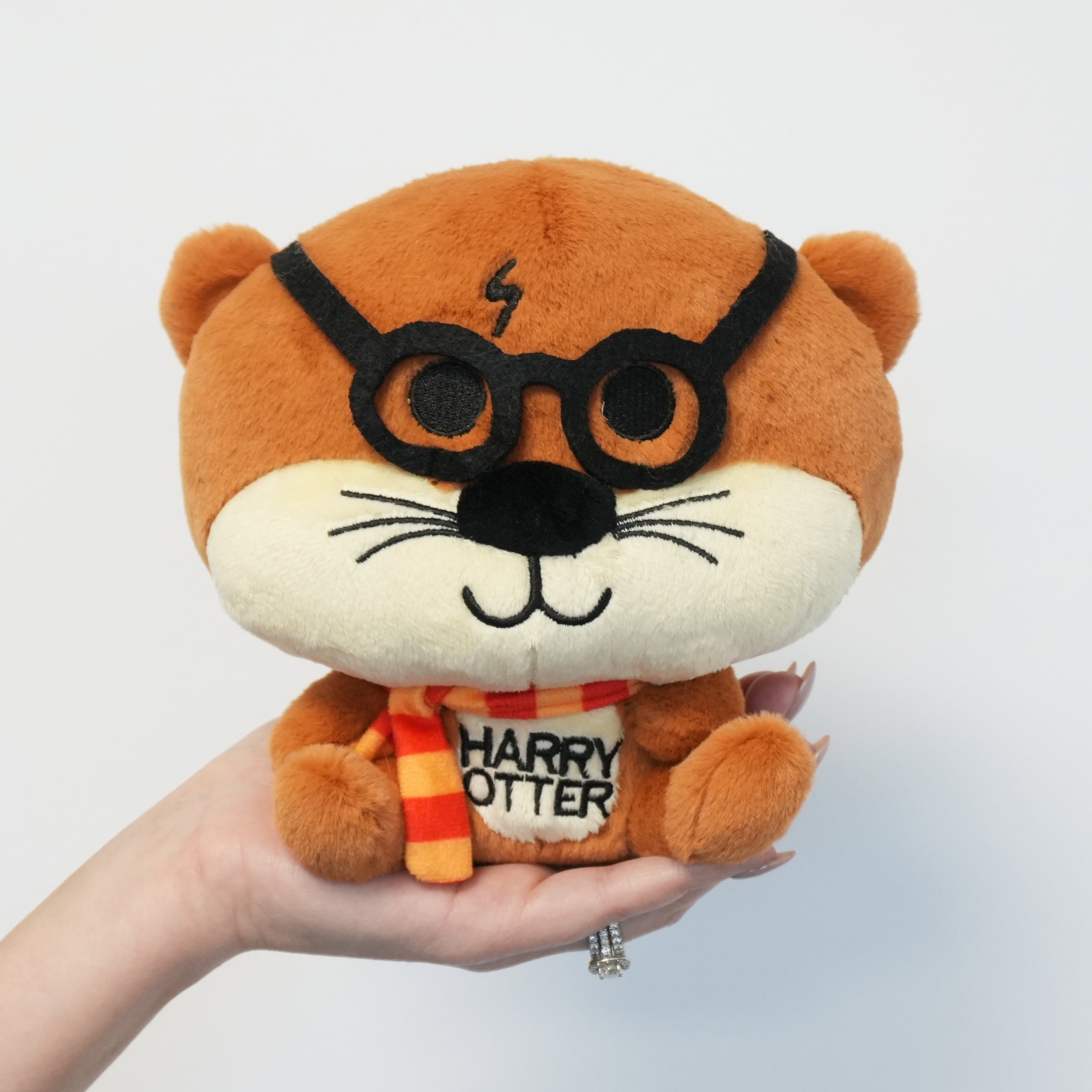 Plush toy of an otter resembling a character from 'Harry Potter' held in a hand against a white background