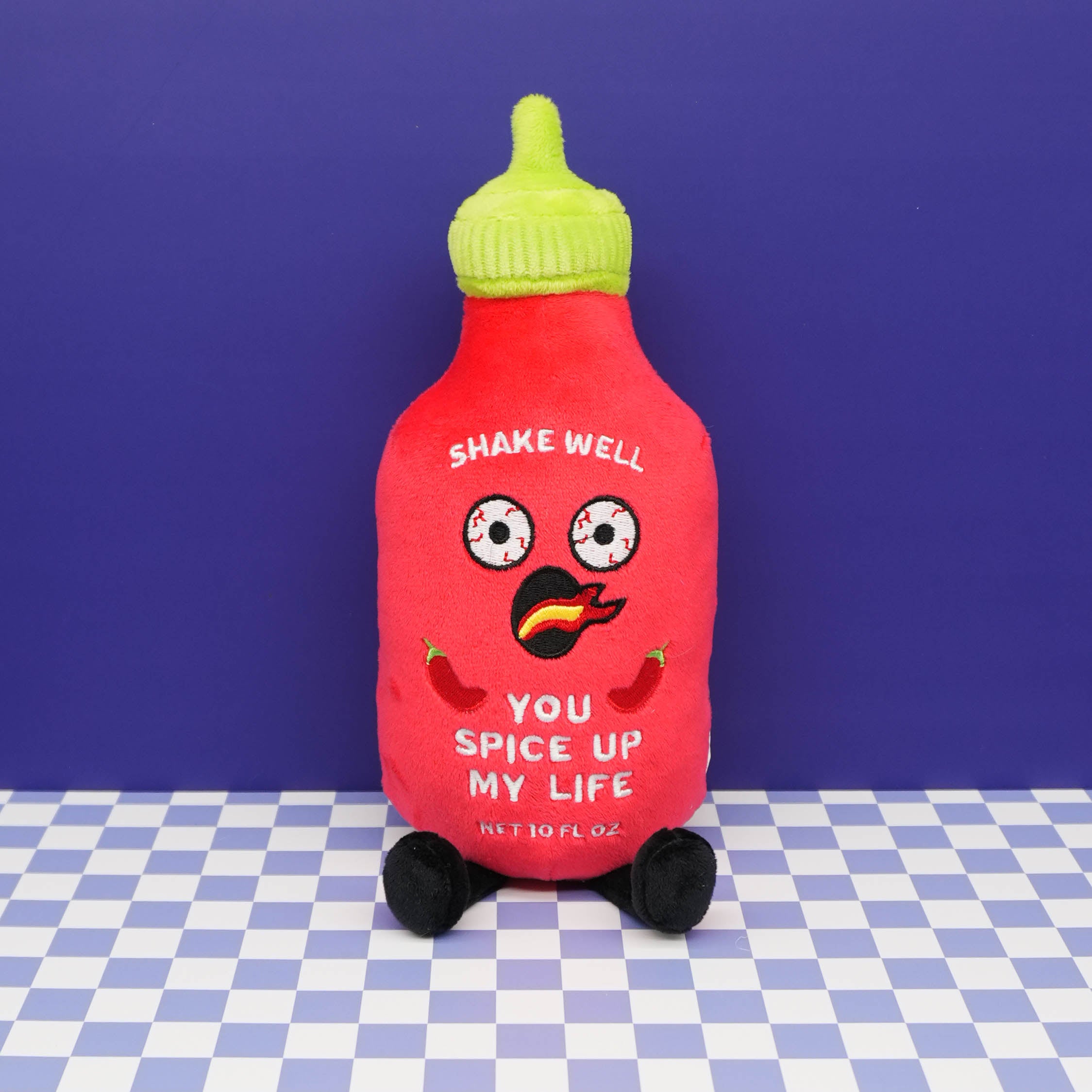 Plush toy resembling a hot sauce bottle with a face on a checkered blue background.