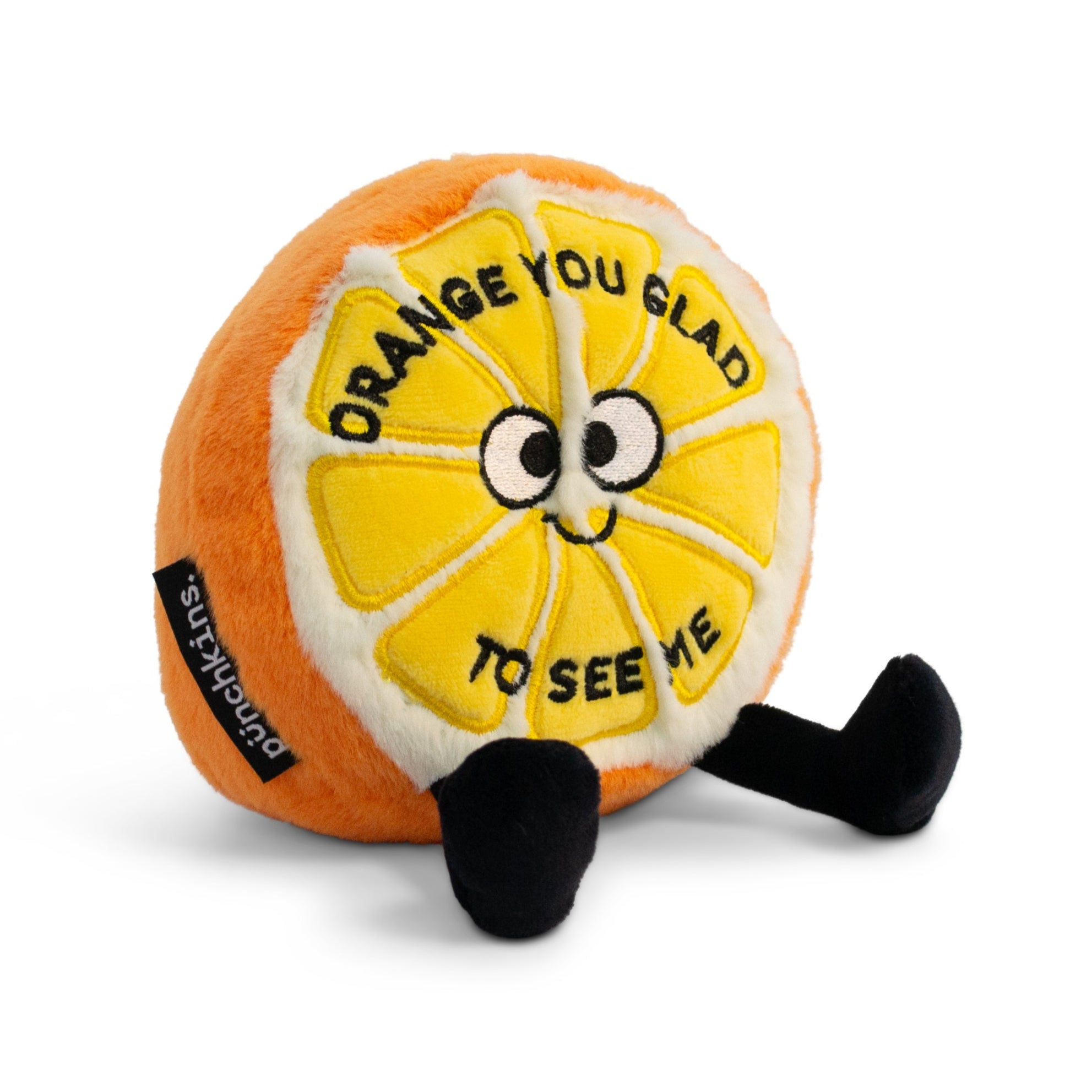 A plush designed to look like an orange with a smiling face and the phrase 'orange you glad to see me' written on it.
