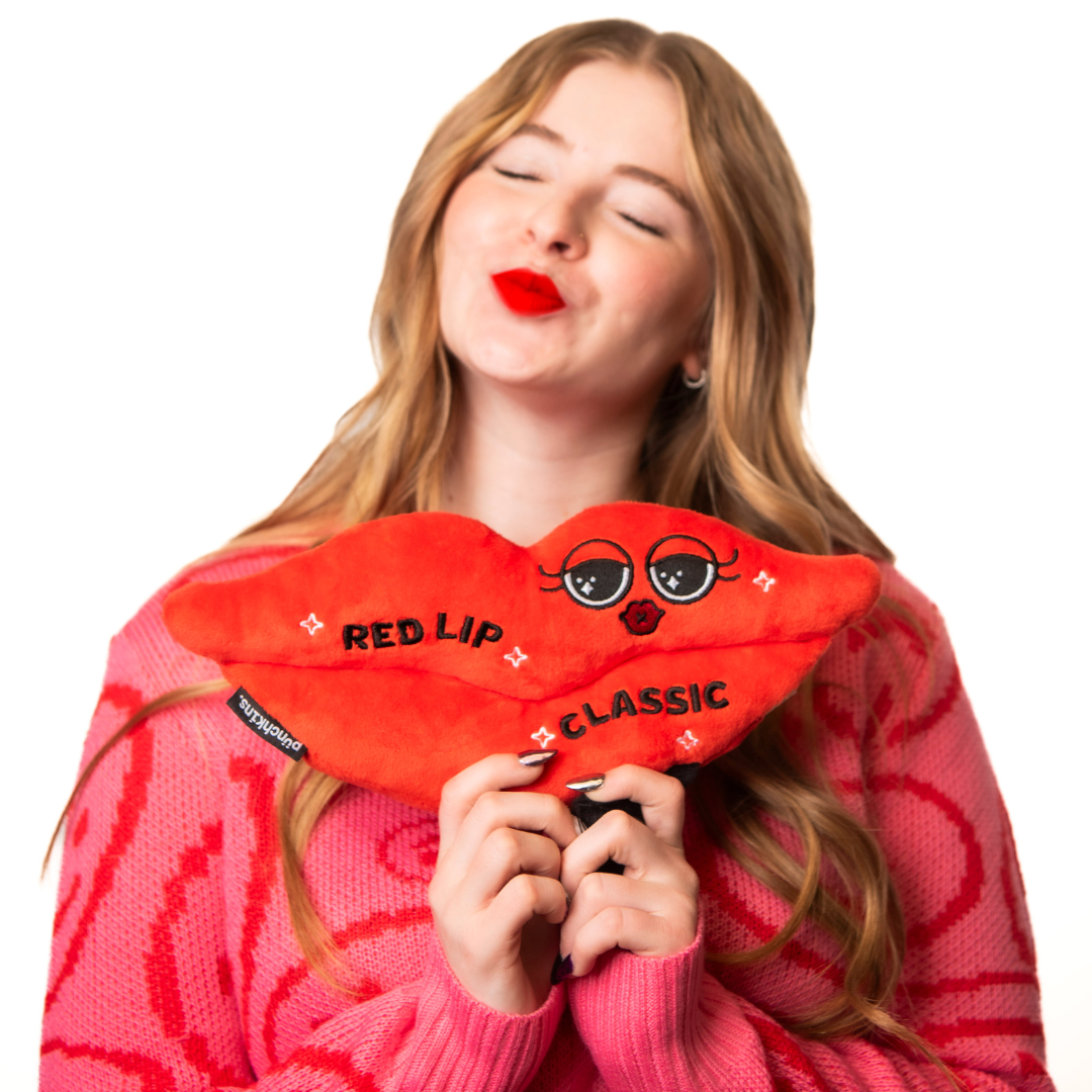 A model holding a plush designed to look like a red lip with "Red lip classic" written on it placed on a couch.