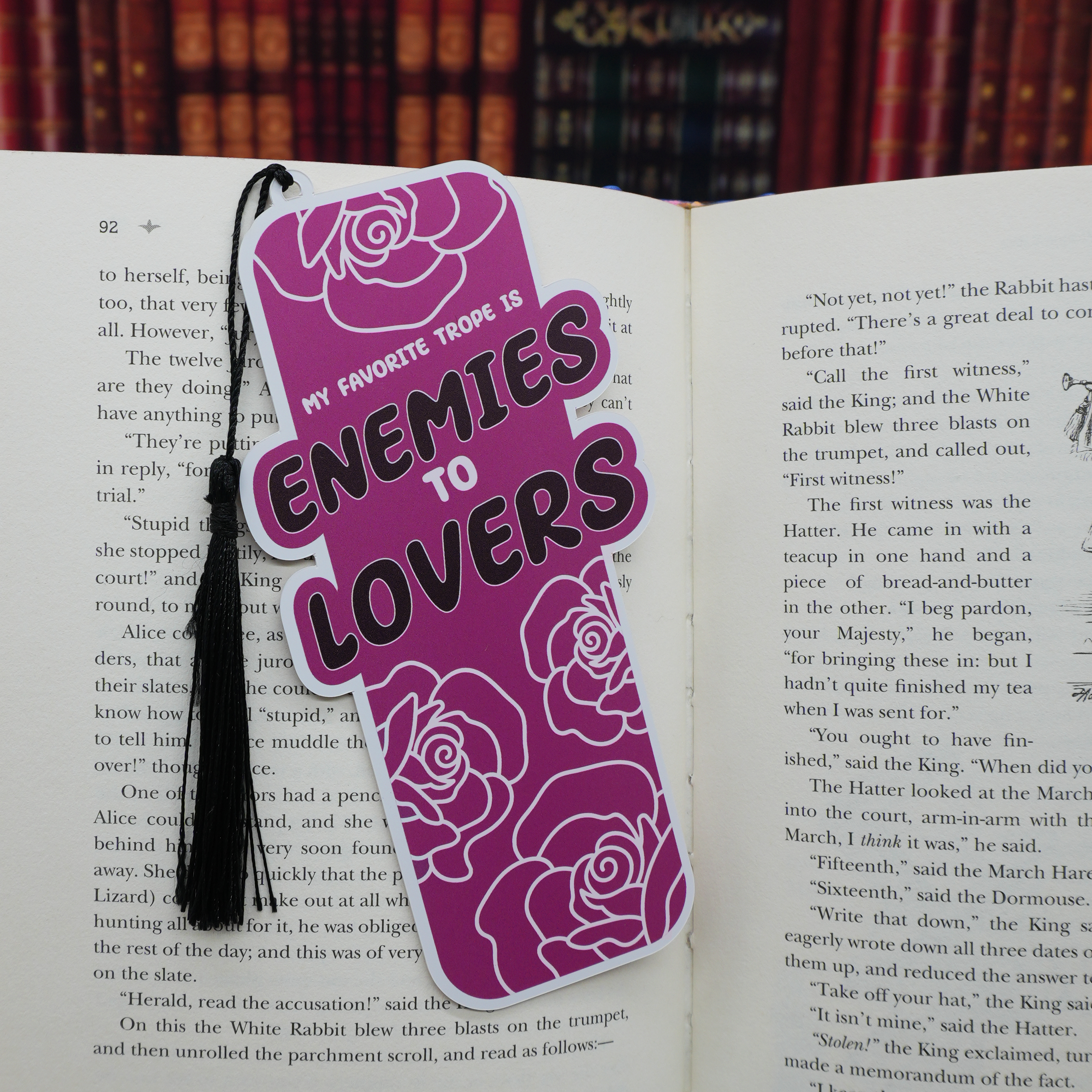 Purple bookmark with floral designs and 'enemies to lovers' text on an open book