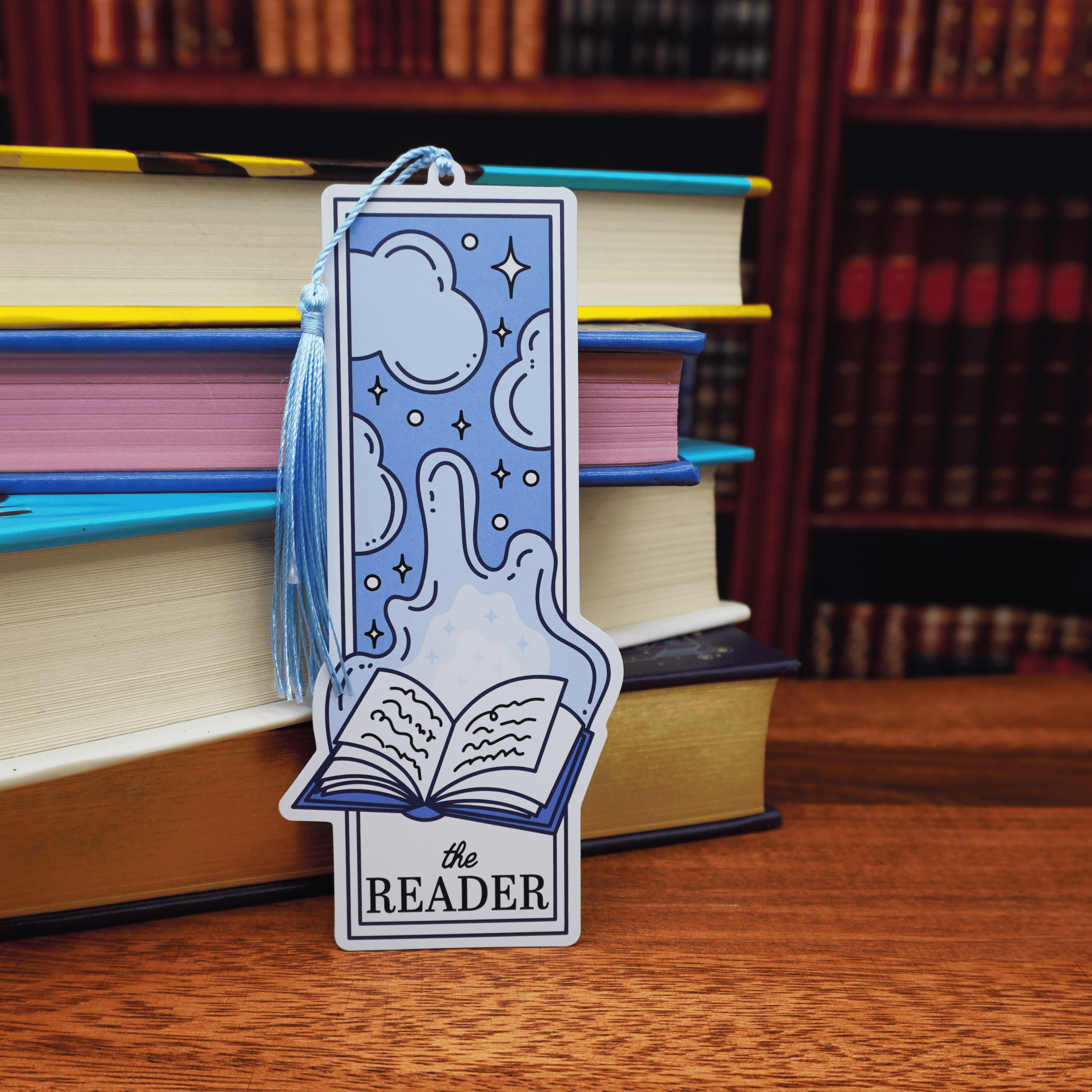 Decorative bookmark with 'the READER' text on a stack of books.