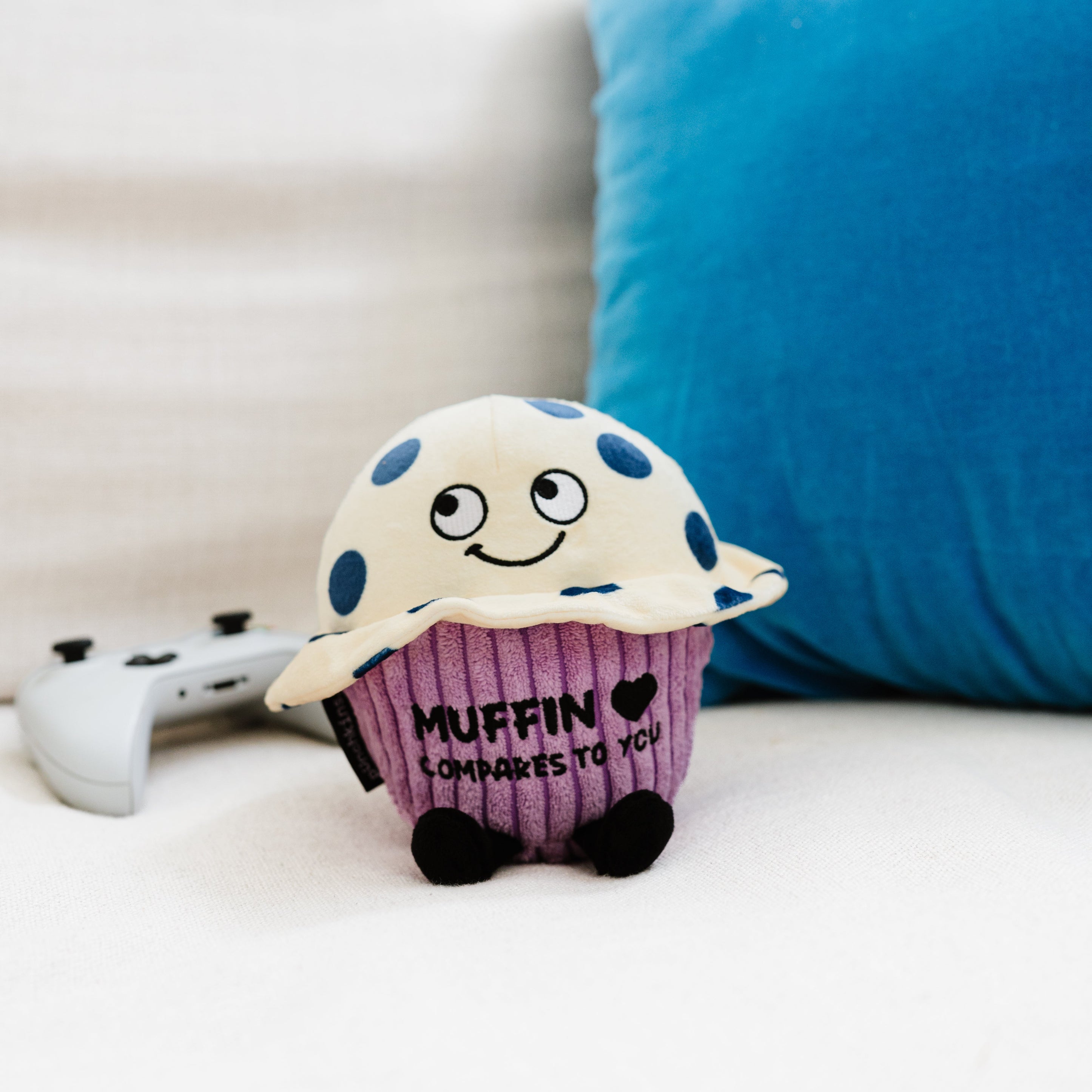 A plush muffin with the text 'MUFFIN COMPARES TO YOU' printed on it placed on a couch.