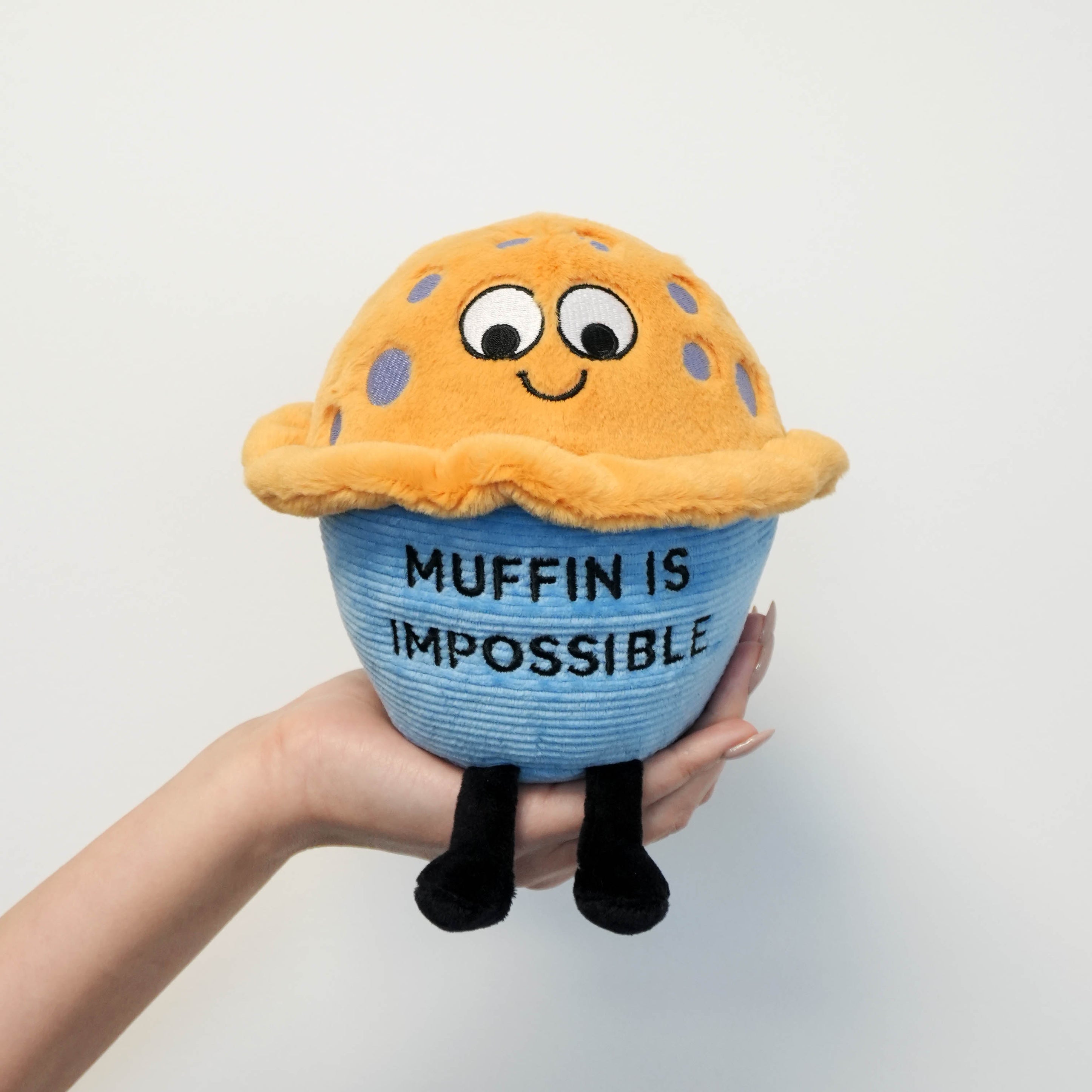 Plush toy resembling a blue muffin with text 'Muffin is Impossible' held by a hand against a white background