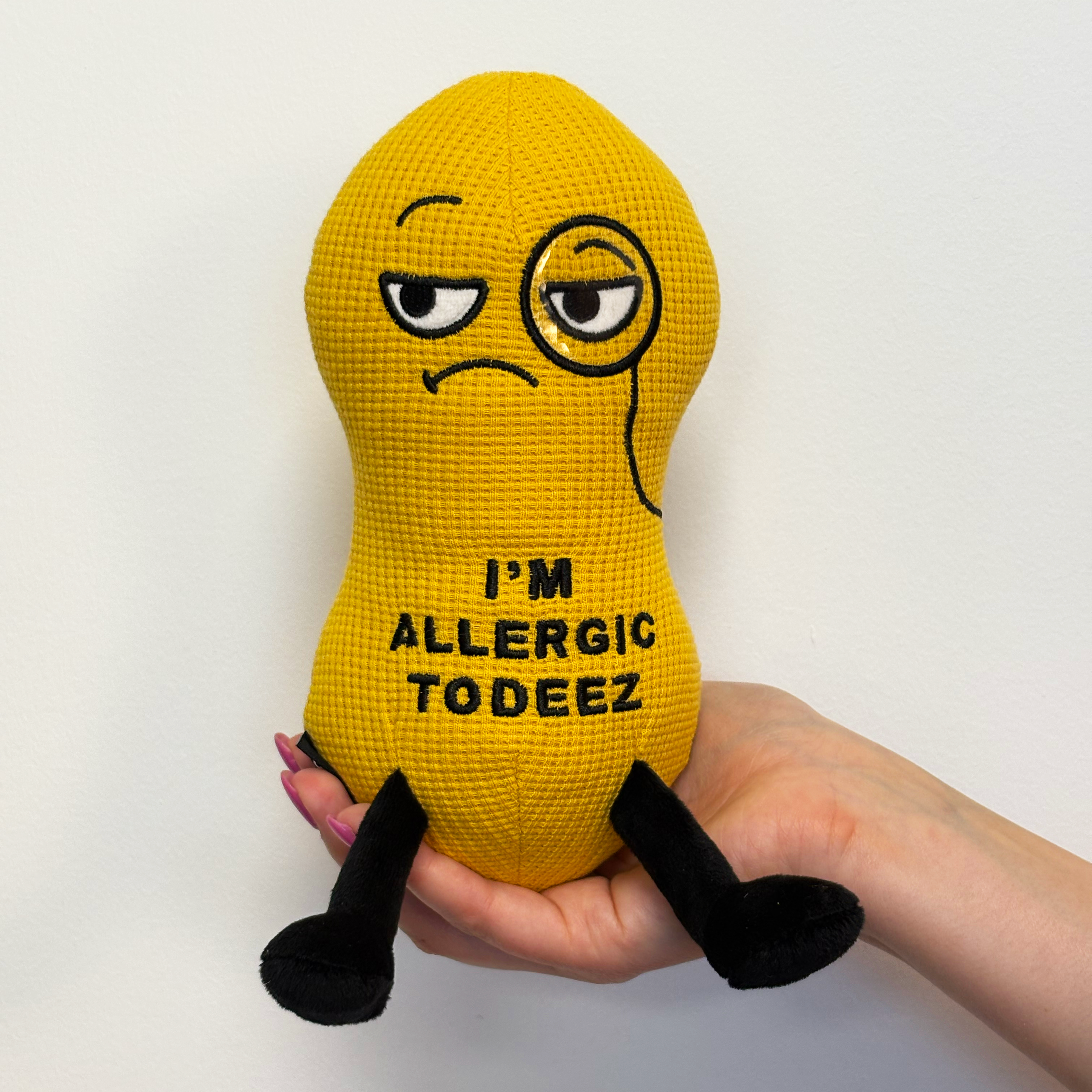 Hand holding peanut plush with the text 'I'm allergic to deez' embroidered on it.