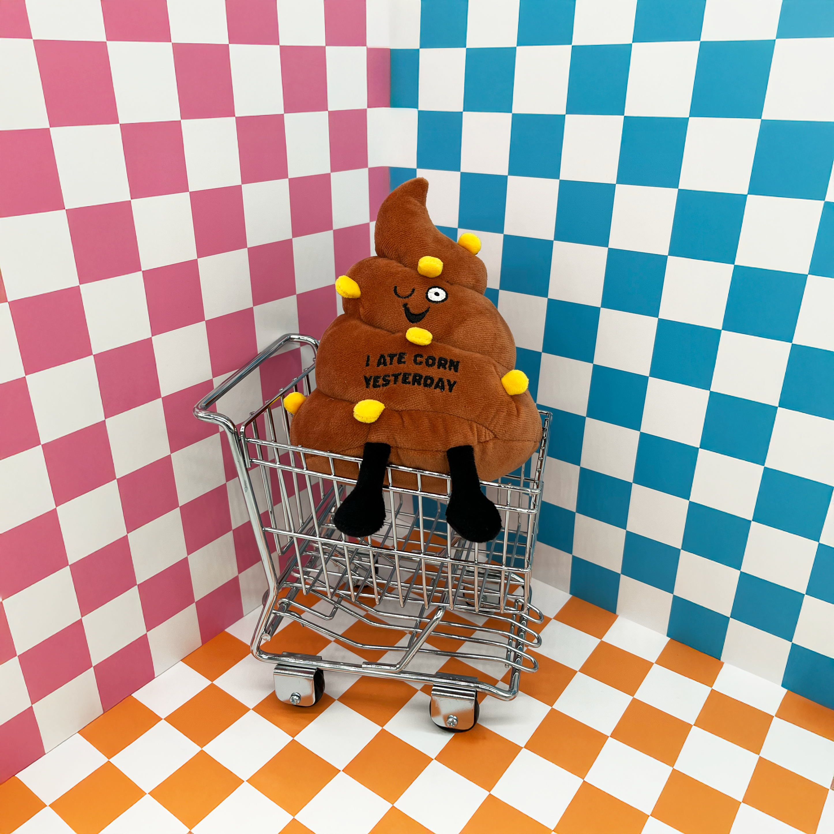 A plush poop with text that reads 'I ATE CORN YESTERDAY' placed in a mini shopping cart.