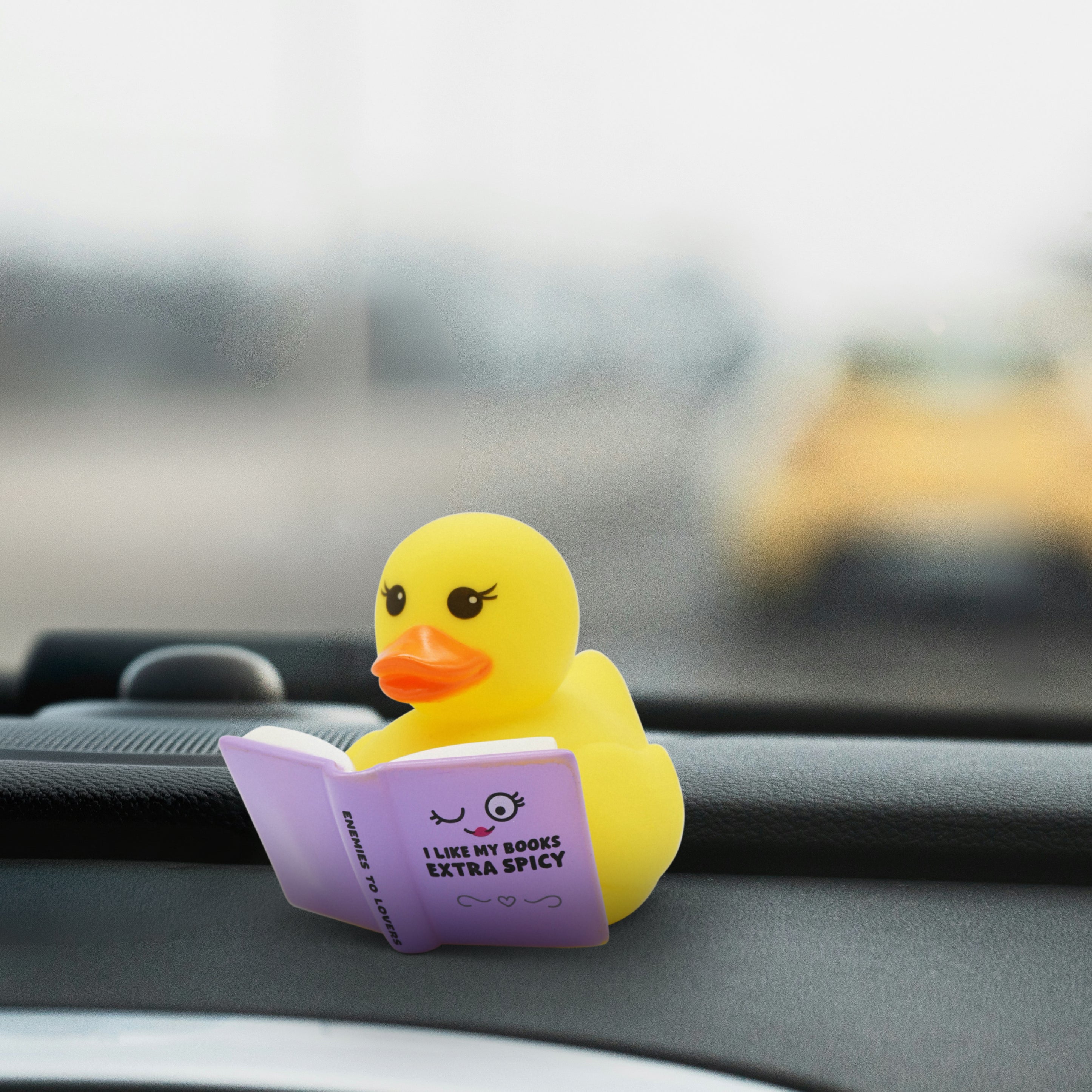 Yellow rubber duck reading a spicy romance book on a car dashboard
