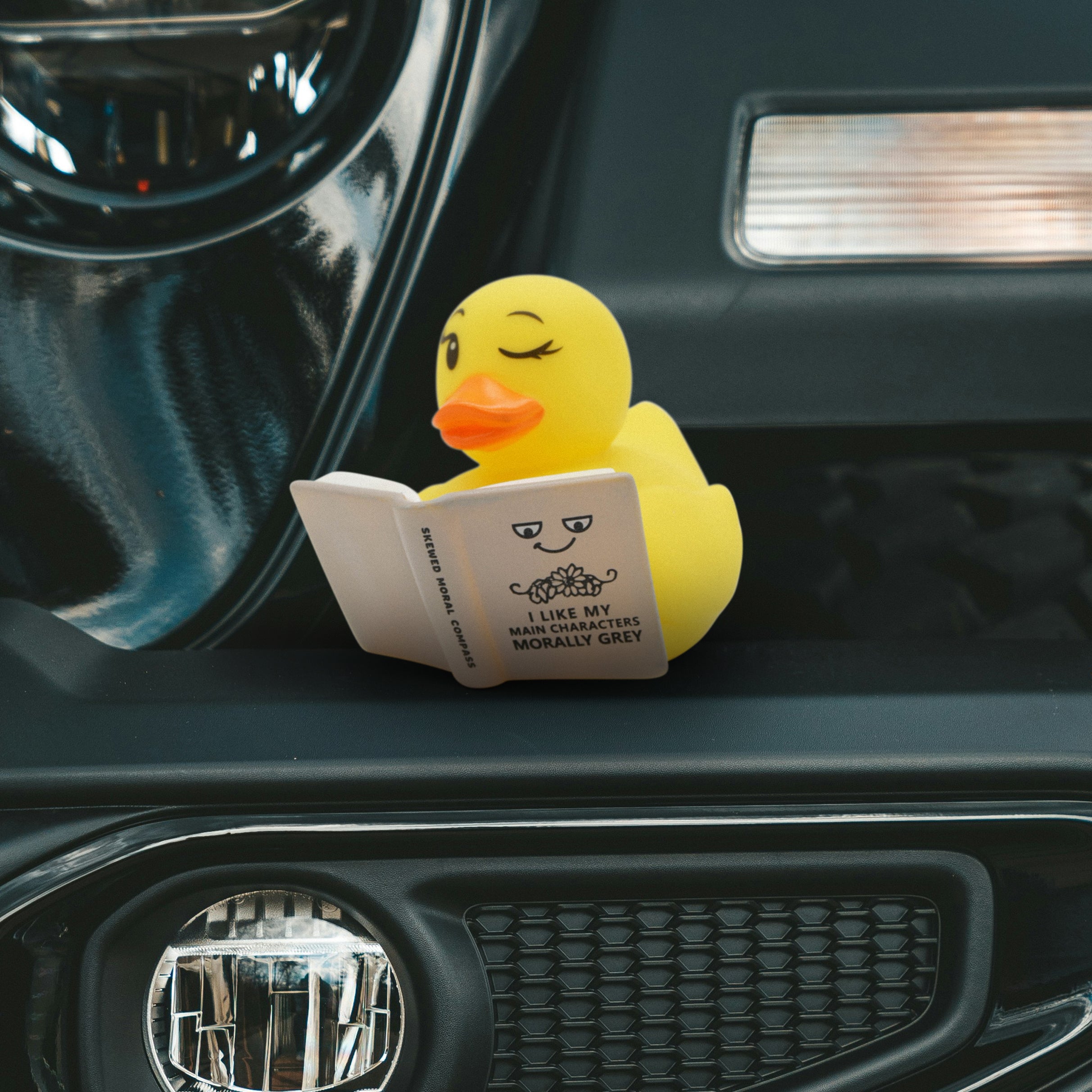 Yellow rubber duck reading a book inside a car.