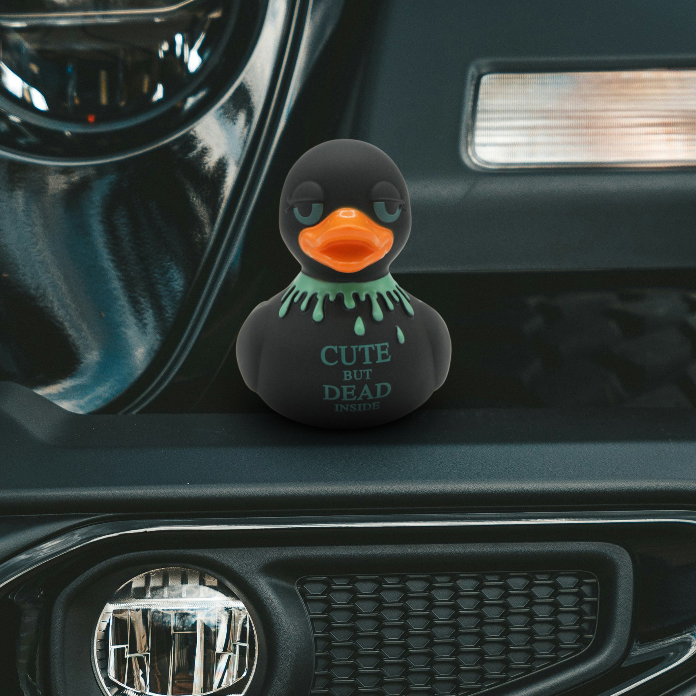 Black rubber duck "cute but dead inside" text on a car dashboard