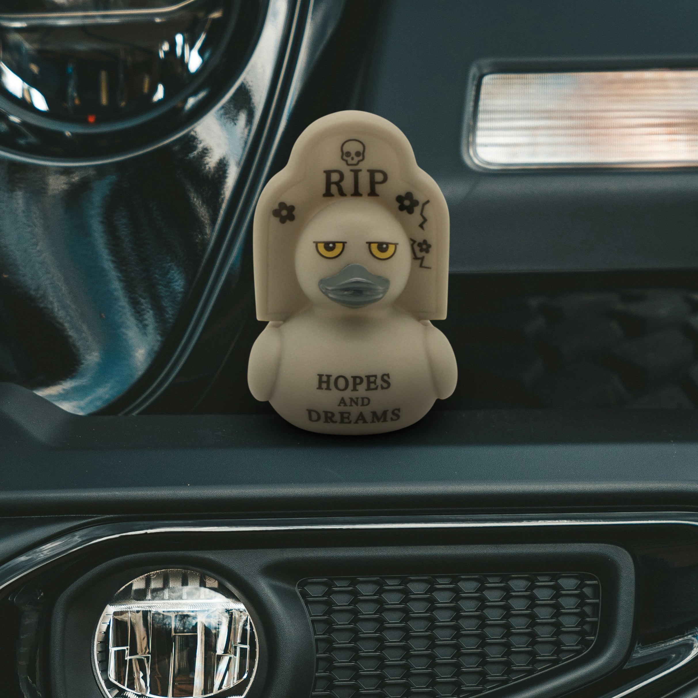 Decorative rubber duck with 'RIP Hopes and Dreams' text on a car dashboard.