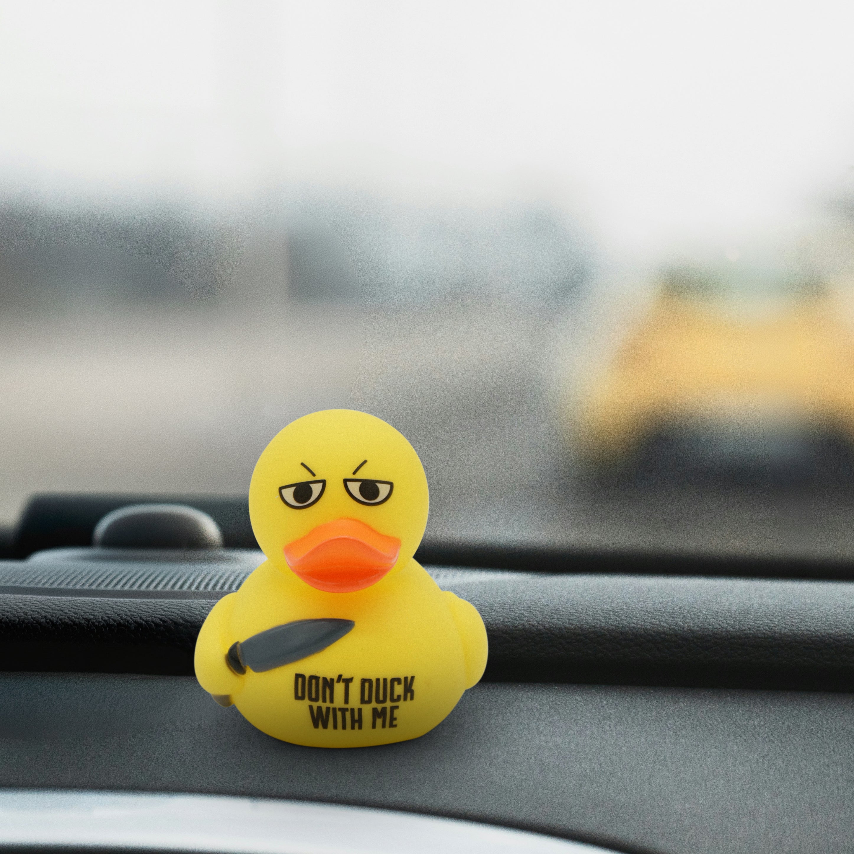 Yellow rubber duck with an angry expression and a knife, with text 'Don't Duck With Me' on a car dashboard.