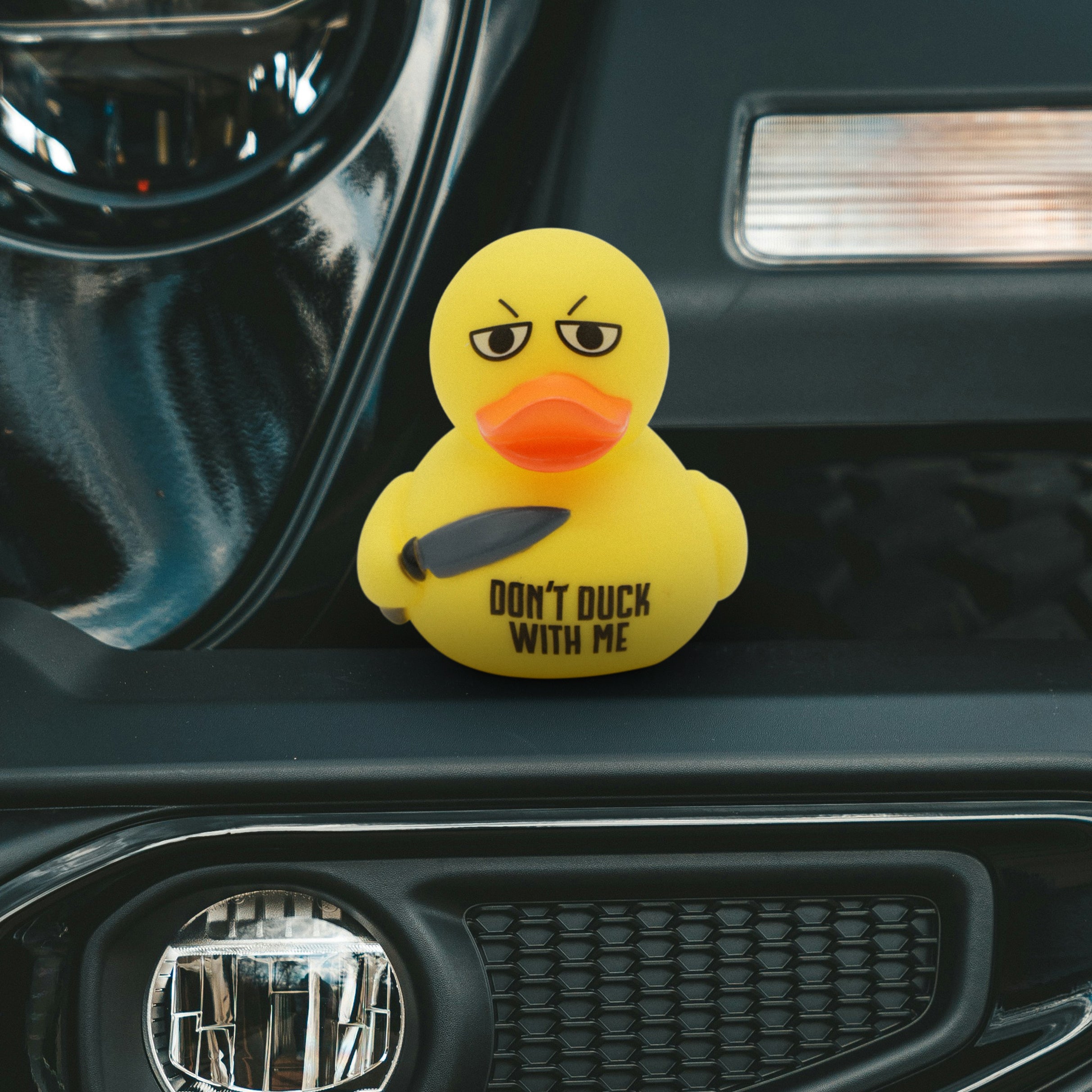 Yellow rubber duck with a serious expression and text 'Don't Duck With Me' on a car dashboard.