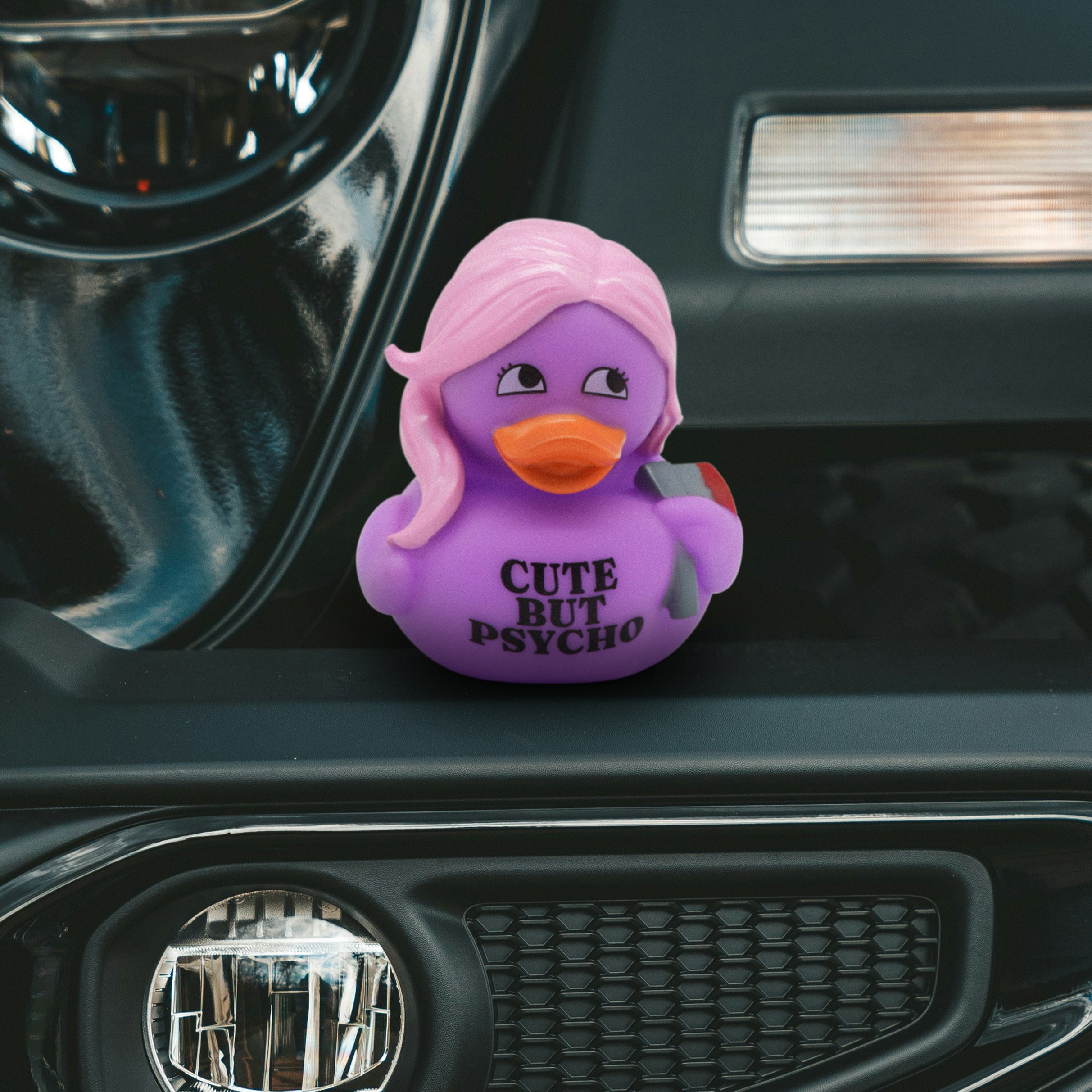 Purple duck-shaped car accessory that reads "cute but psycho" on a car dashboard.