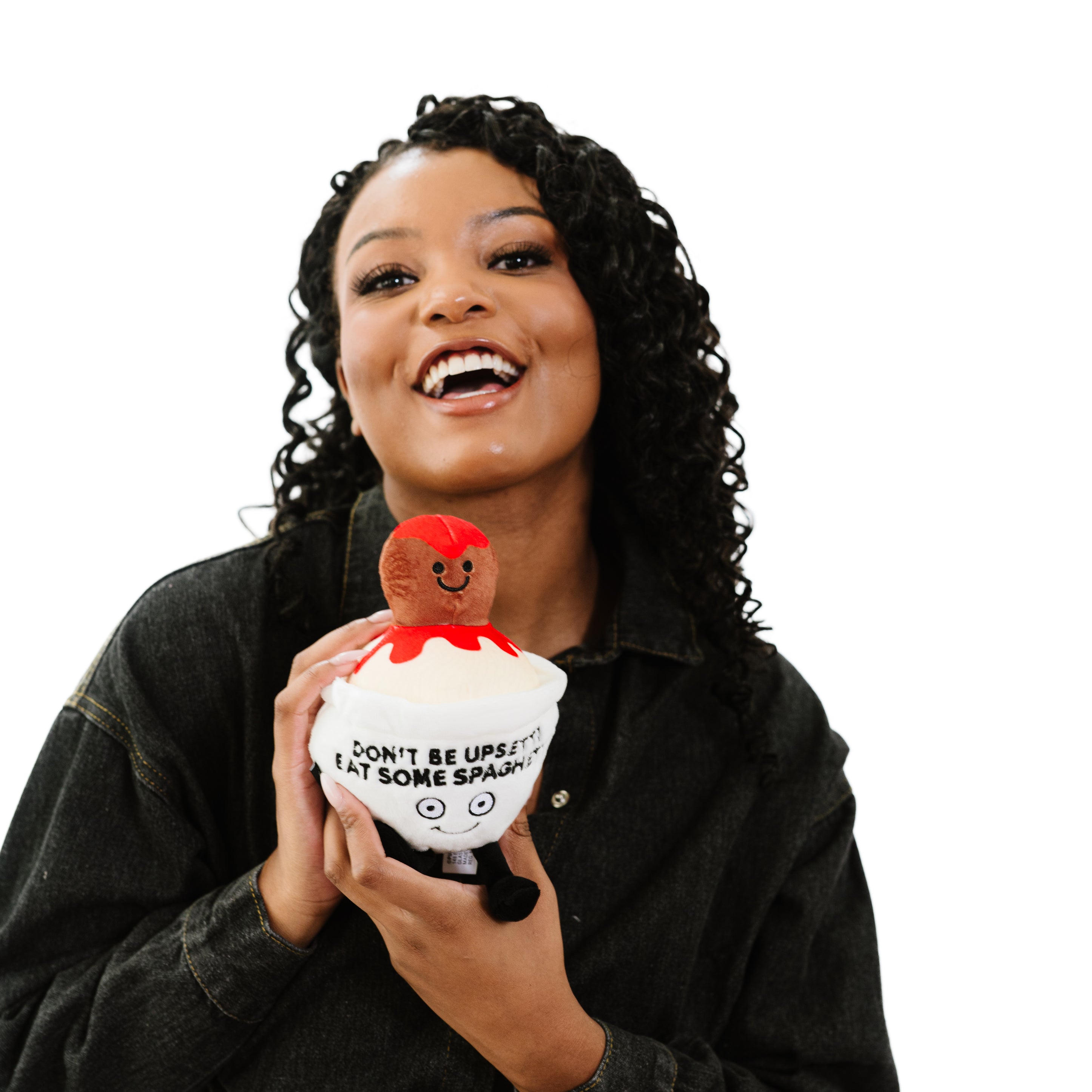 A woman holding a plush resembling a bowl of spaghetti with a smiling meatball on top that reads, 'DON'T BE UPSETTI EAT SOME SPAGHETTI'.