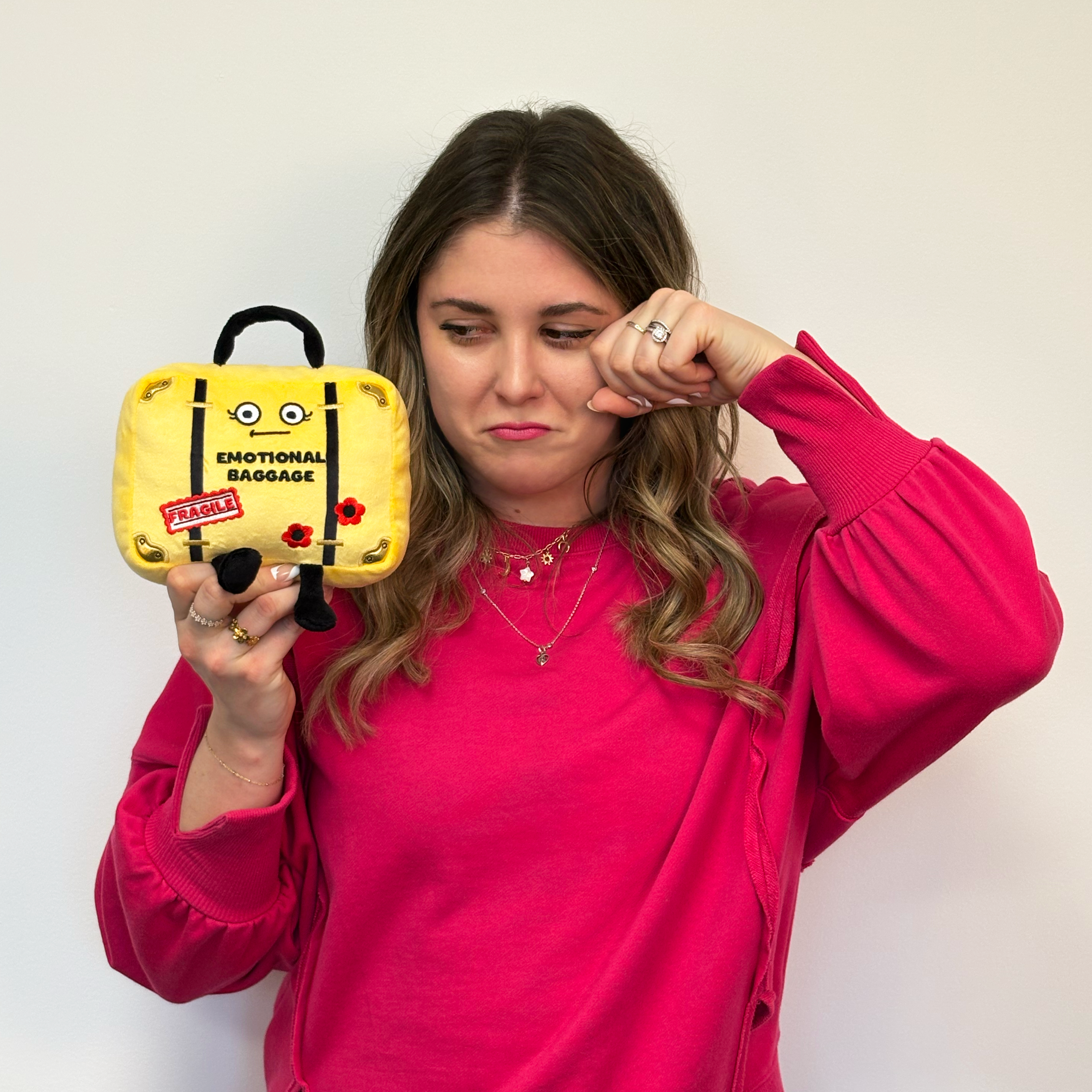 Woman holding a small yellow suitcase with 'Emotional Baggage' text against a plain background
