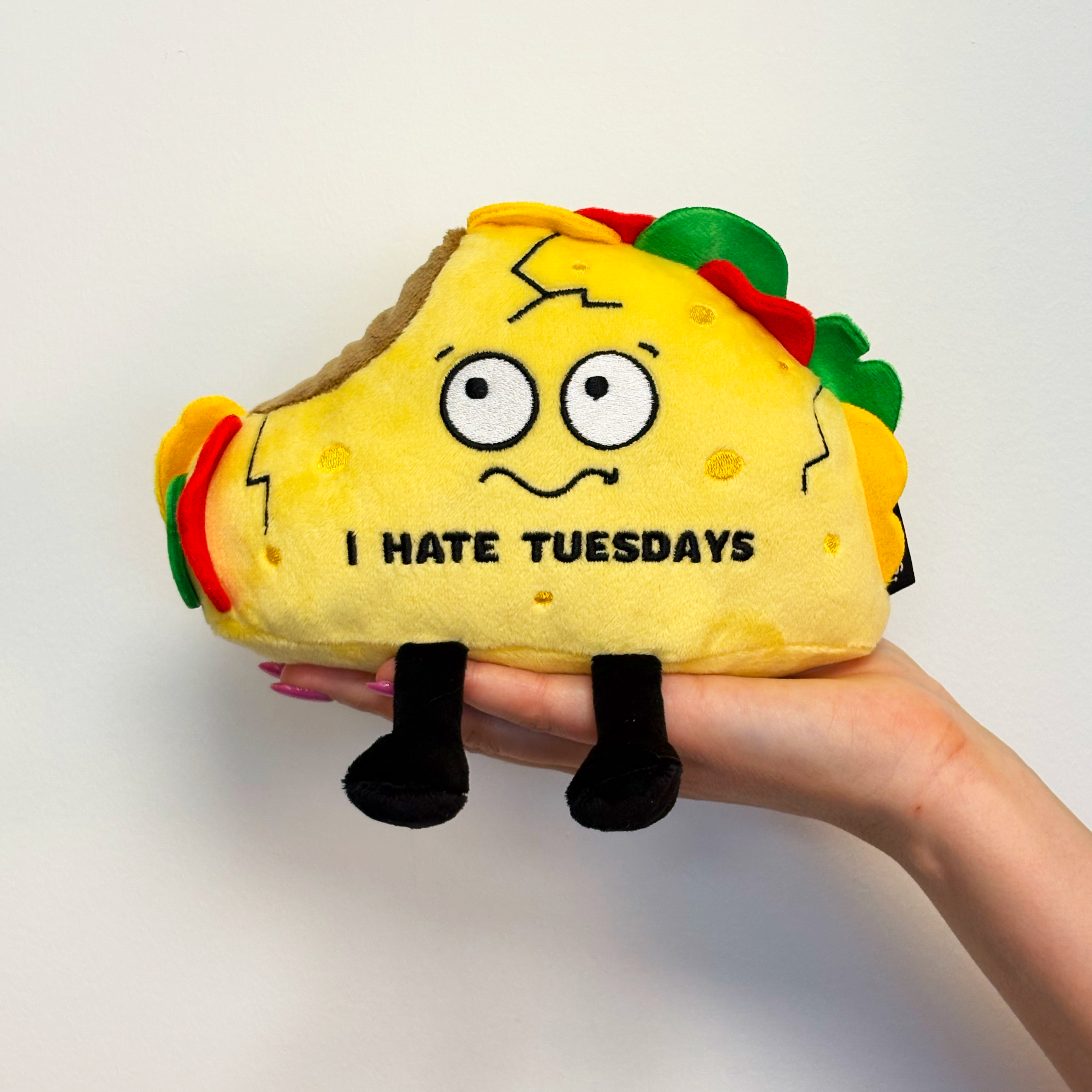 A hand holding a plush taco with the text 'I HATE TUESDAYS' embroidered on it.