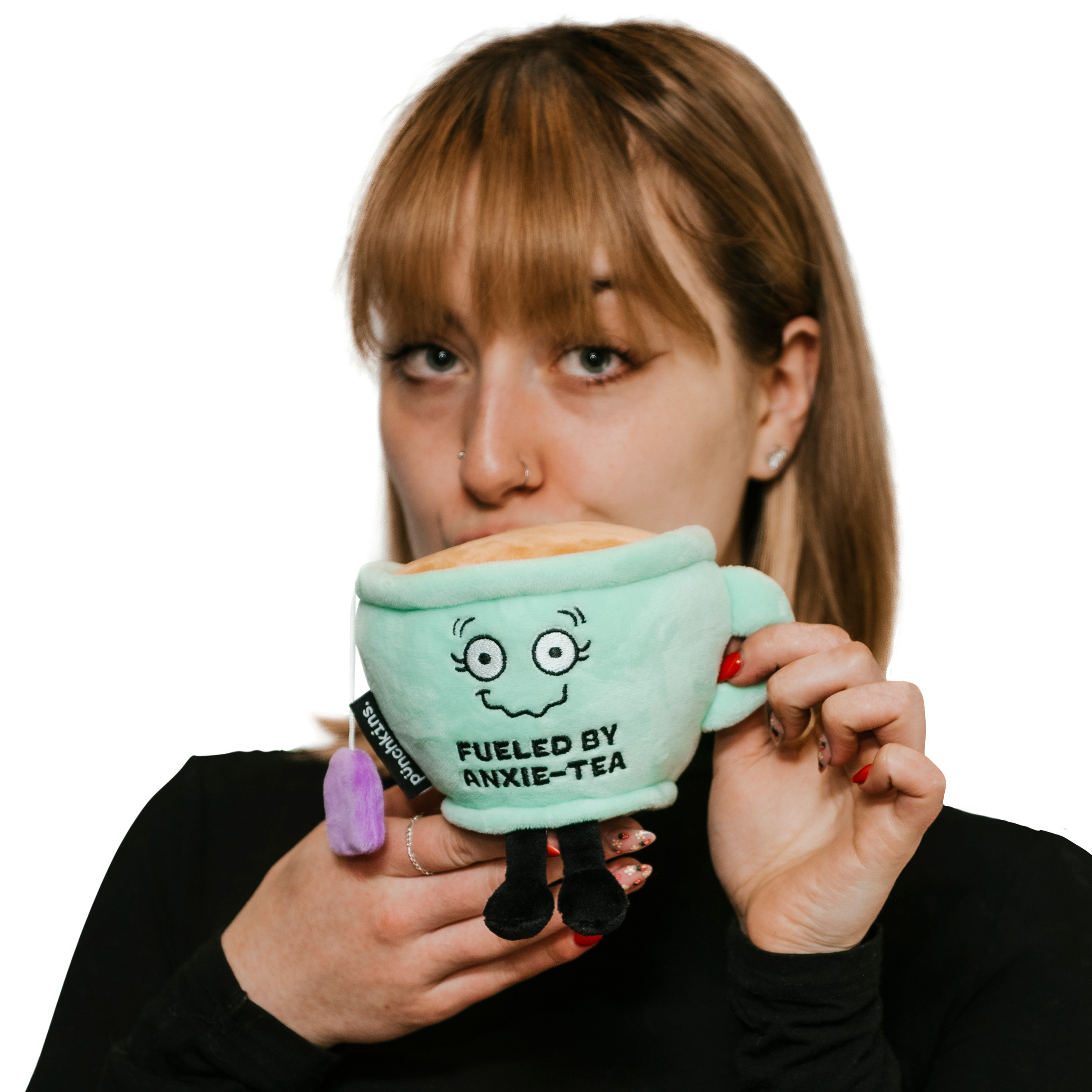 A woman holding a plush designed to look like a teacup with a face and text that reads 'FUELED BY ANXIE-TEA'.