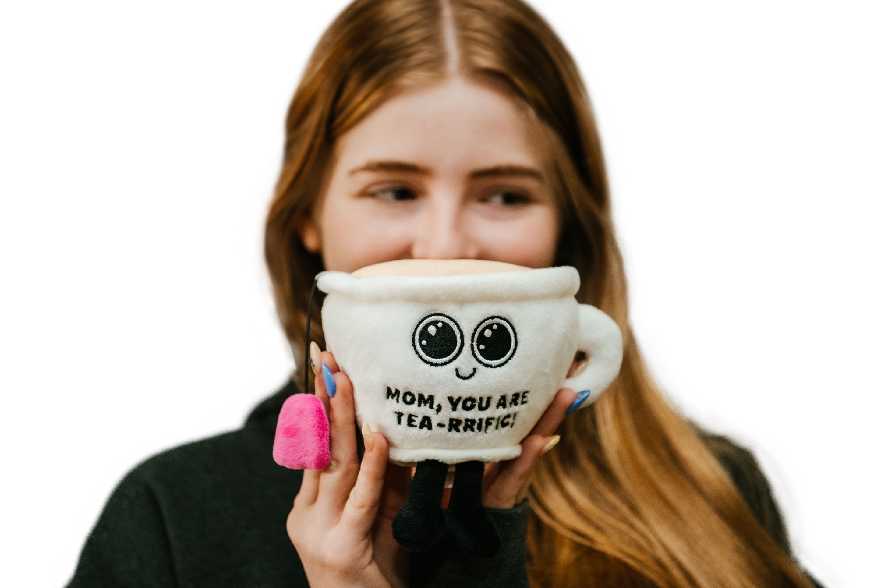 A woman holding a plush teacup with a face, eyes and the text 'MOM, YOU ARE TEA-RRIFIC' is visible on it.