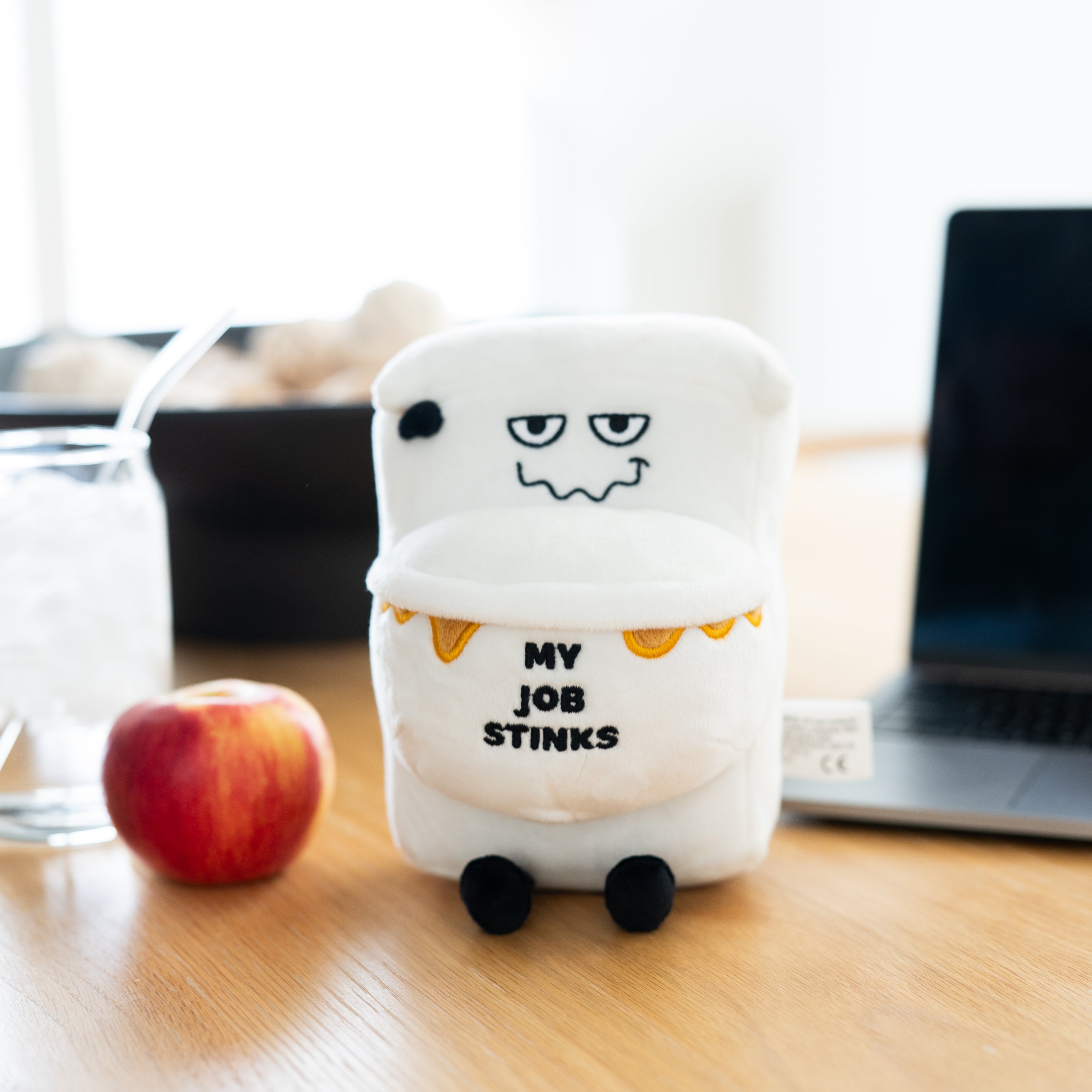 A plush designed to resemble a dirty toilet with the text 'My job stinks' written on it placed on a kitchen table.