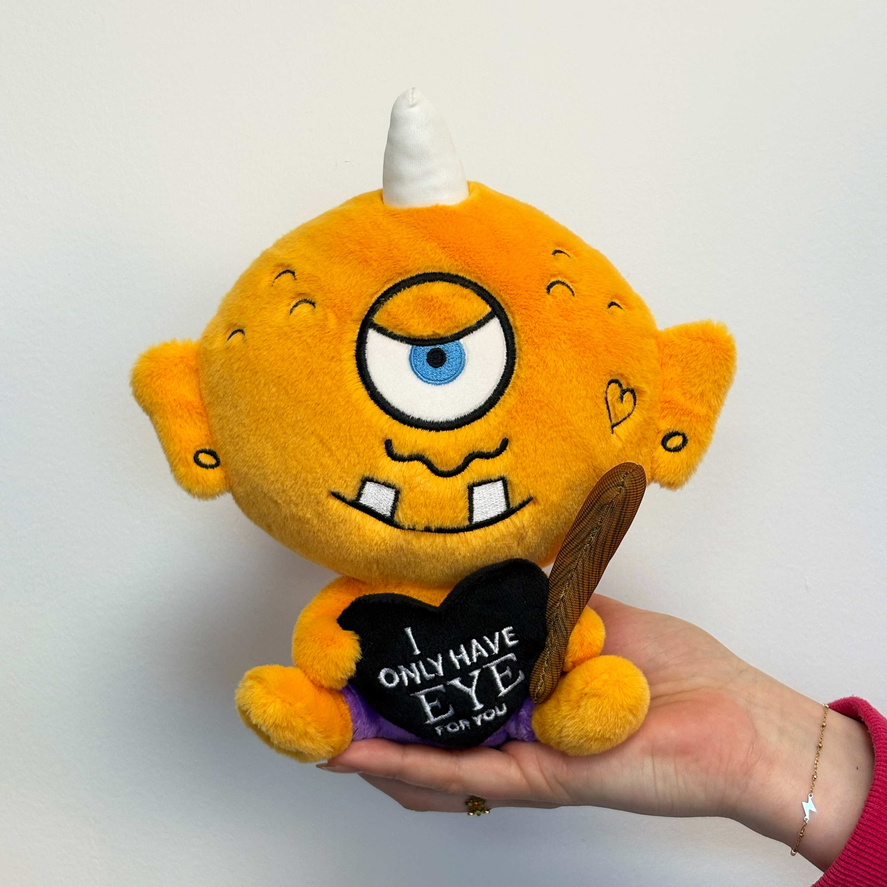 A hand holding a cyclops plush toy that reads, "I only have eye for you."