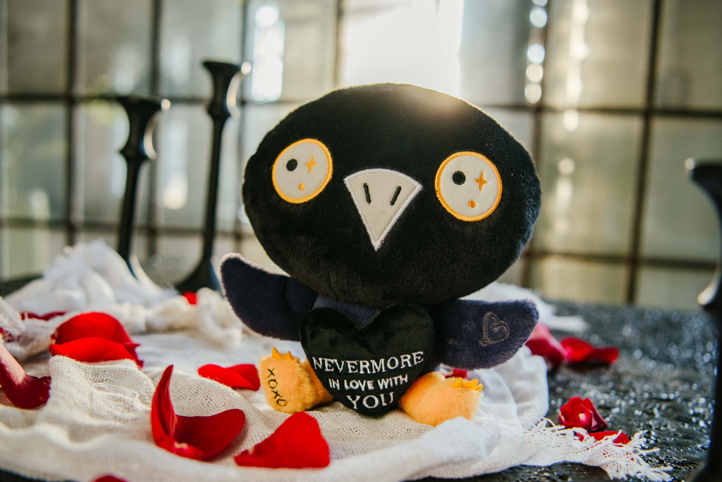 Raven plush toy sitting on a bed of rose petals