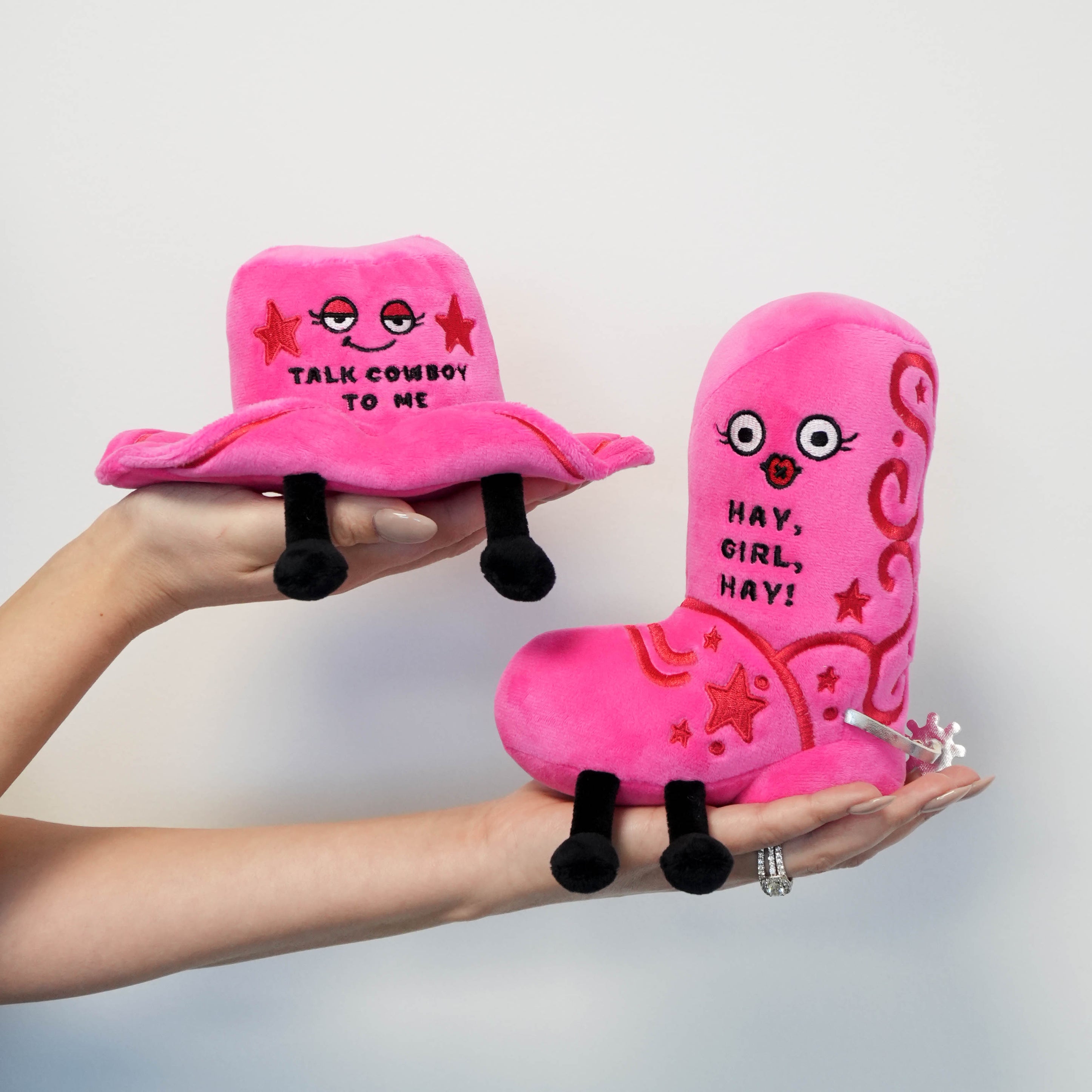 Pink cowboy hat and boot plush toys held in hands against a white background