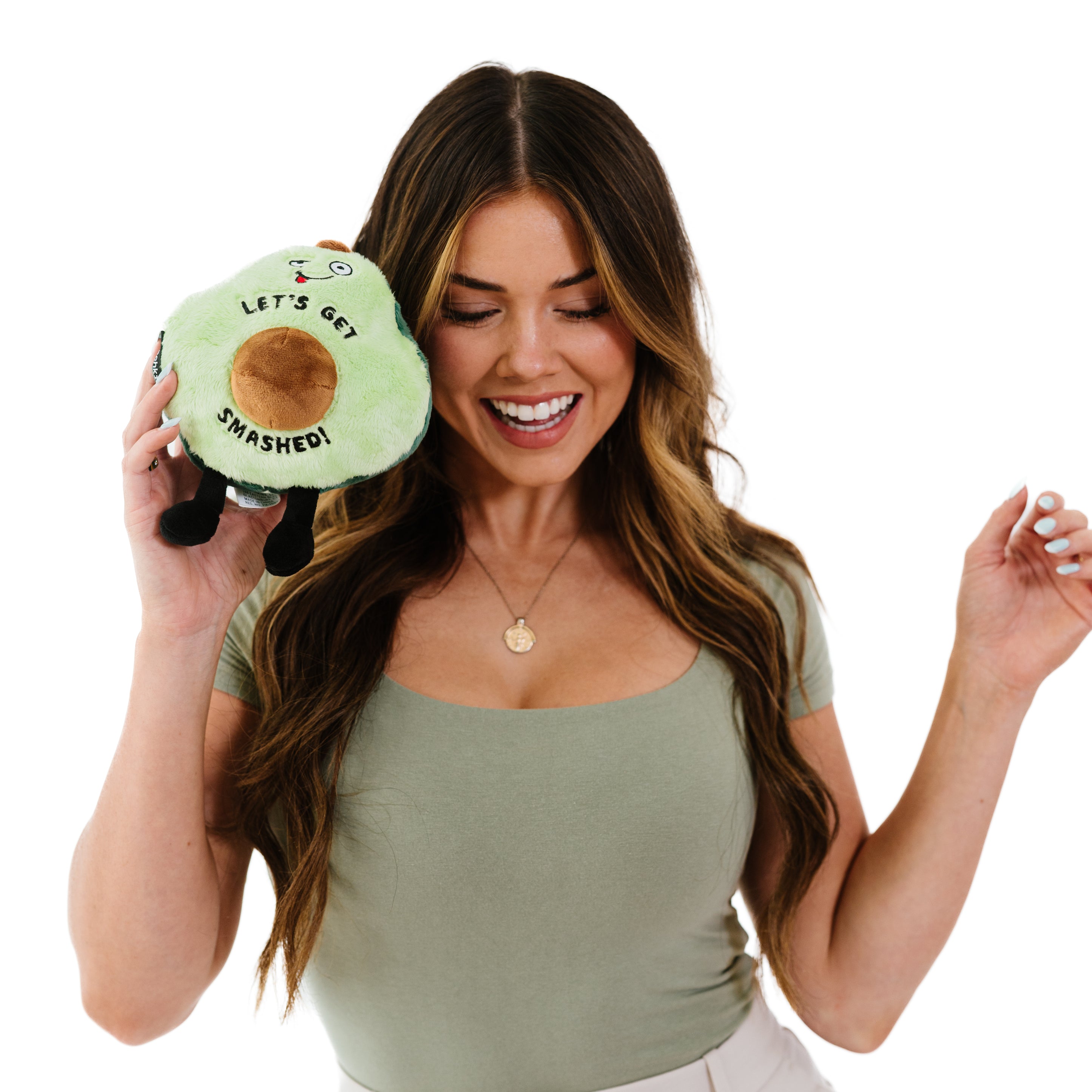 A woman holding a plush resembling an avocado with a smiling face and the phrase 'LET'S GET SMASHED!' printed on it.